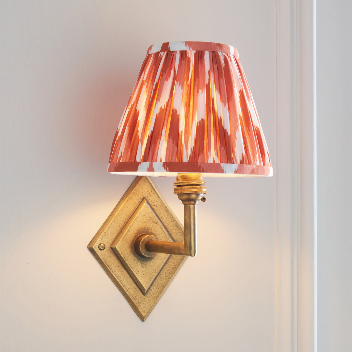 Endon Diamond Angle wall light switched on against a pale wall, the apricot orange zigzag shade glowing above the antique brass angled arm