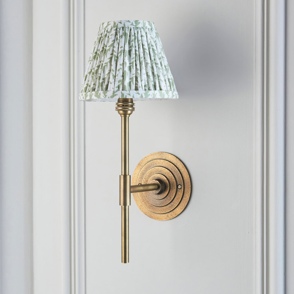 Endon Halo Tall wall light unlit on a pale grey panelled wall, antique brass stem and herb garden green leaf pleated shade