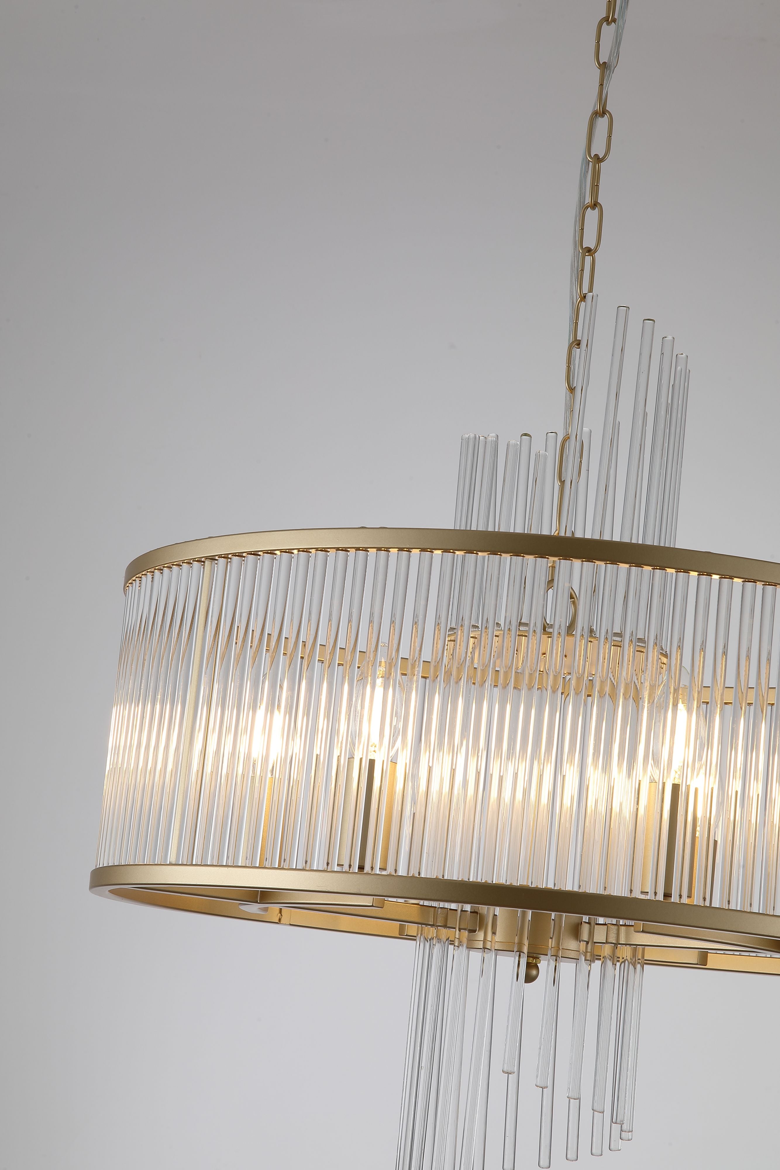Close up of the Lara pendant's brushed gold ring and clear glass rods, showing the candle bulbs glowing inside the fringed shade