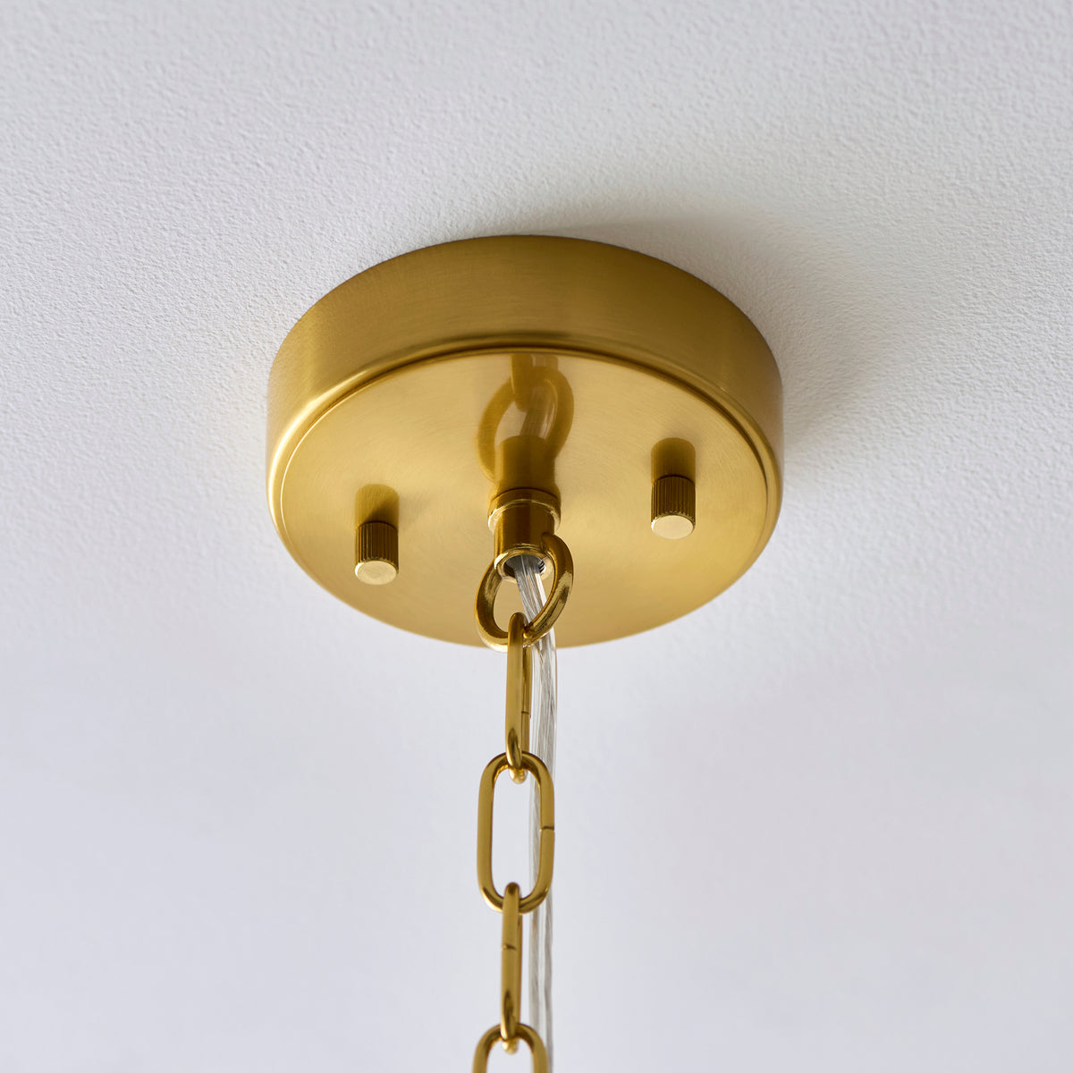 Close up of the brushed aged brass ceiling rose, chain and clear flex on the Endon Montpellier 6 light pendant against a white ceiling