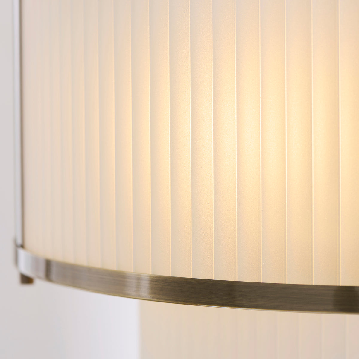 Extreme close up of the frosted ribbed glass texture and antique brass banding on the Endon Ridgeton 5 light tiered pendant, lit from within