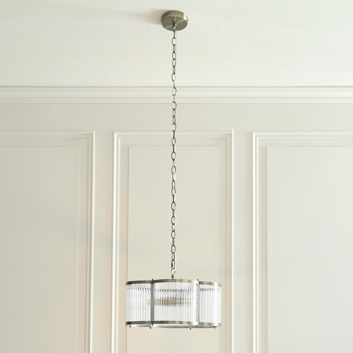 Endon Ridgeton Scallop pendant hanging on its chain against the panelled wall, with a table below holding a vase and bowl.