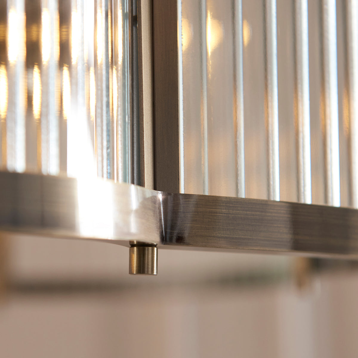 Extreme close up of the Ridgeton Scallop pendant's ribbed glass panel edge and frame joint, backlit with warm light.