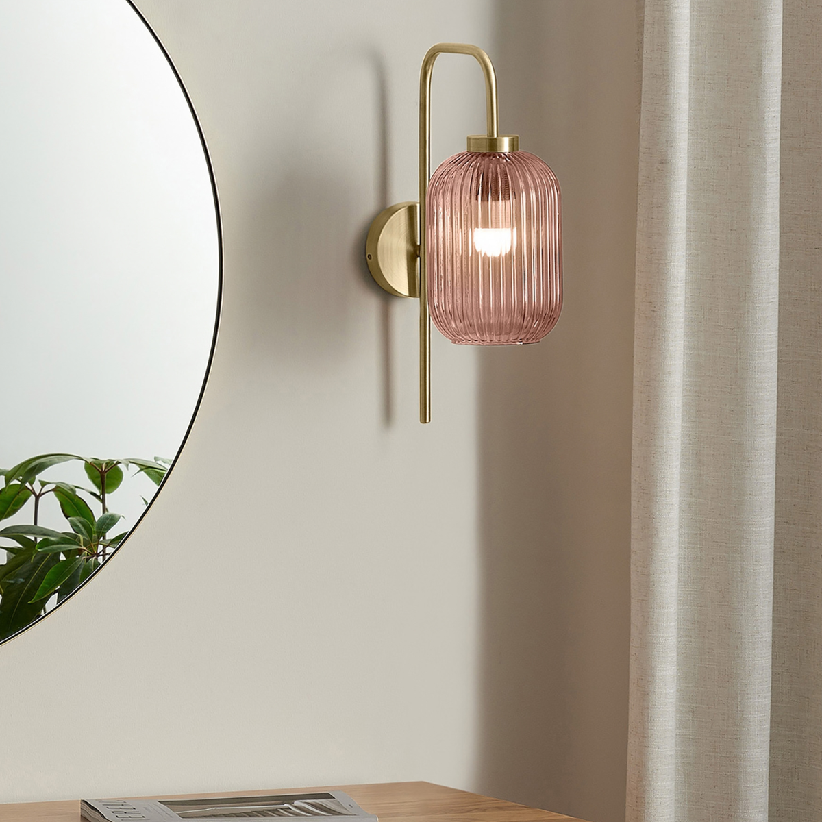 MADE.COM Briz wall light in brushed brass with ribbed pink glass shade, lifestyle shot beside a round mirror