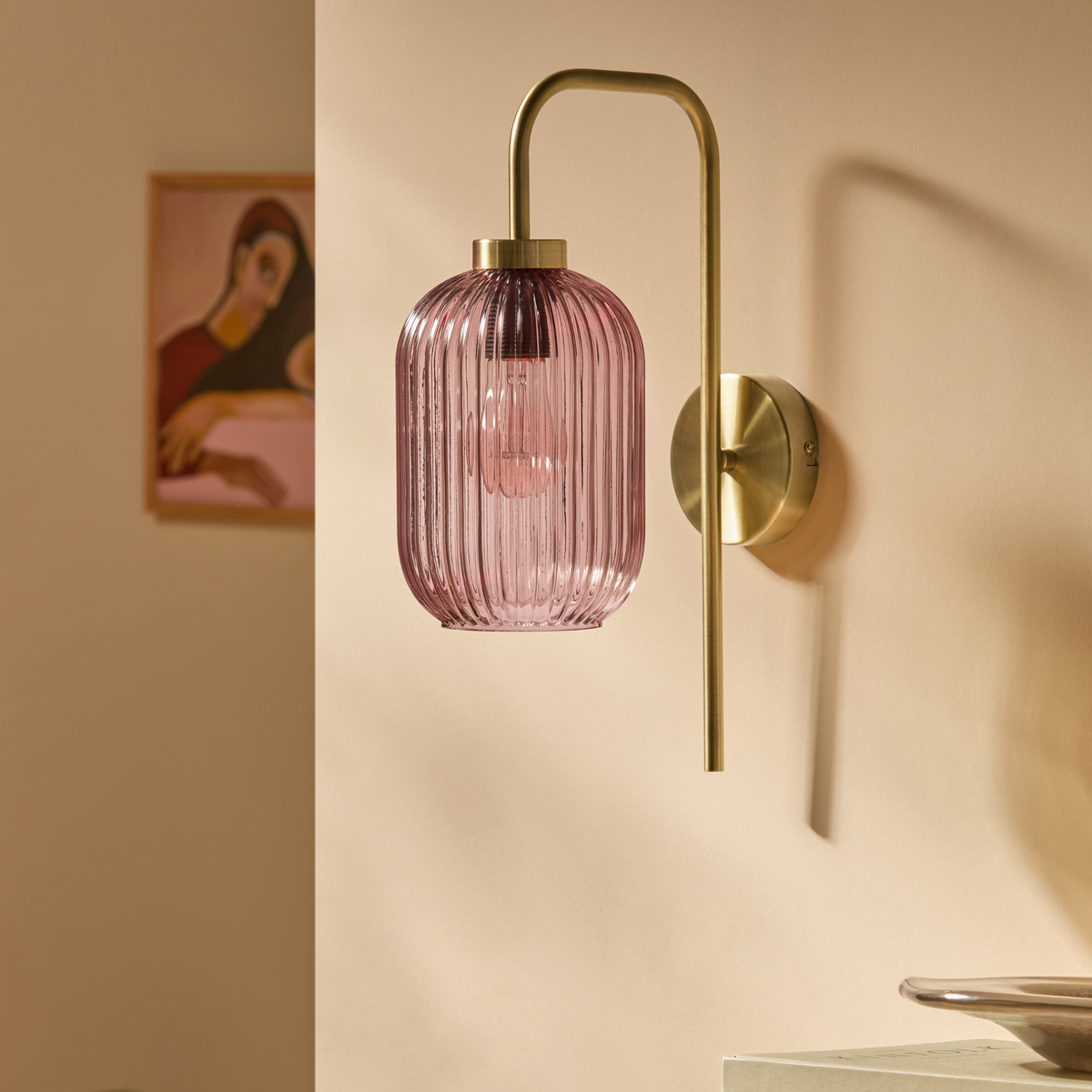 MADE.COM Briz wall light in brushed brass with ribbed pink glass shade, lit on a warm toned wall