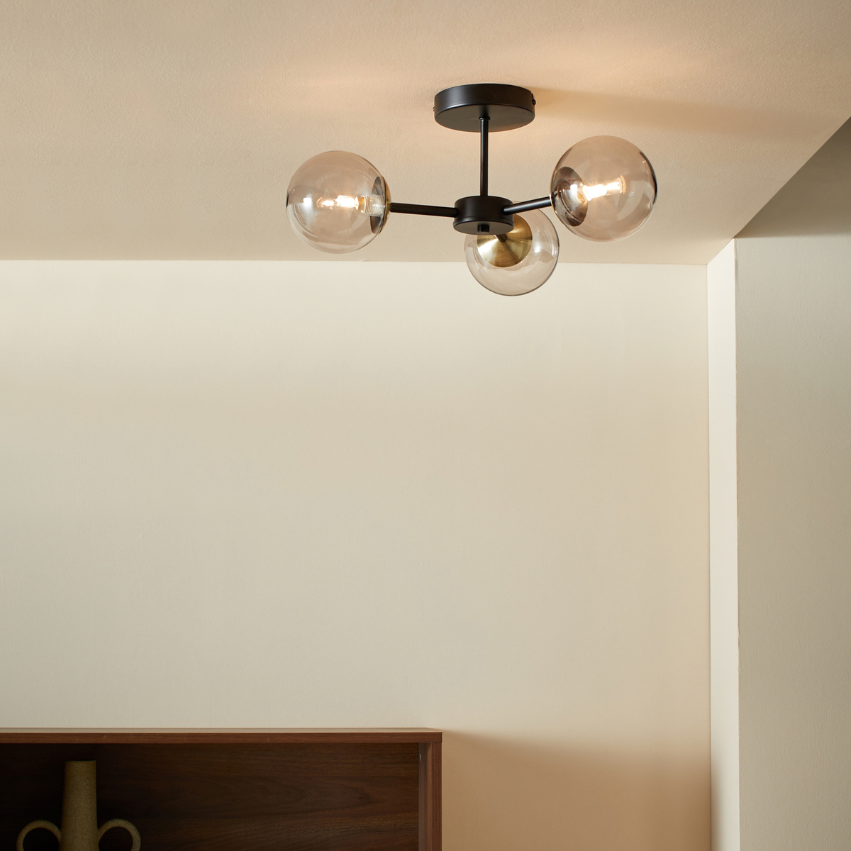 MADE Globe 3 light flush ceiling light in matt black and antique brass, lifestyle shot with tinted glass globes