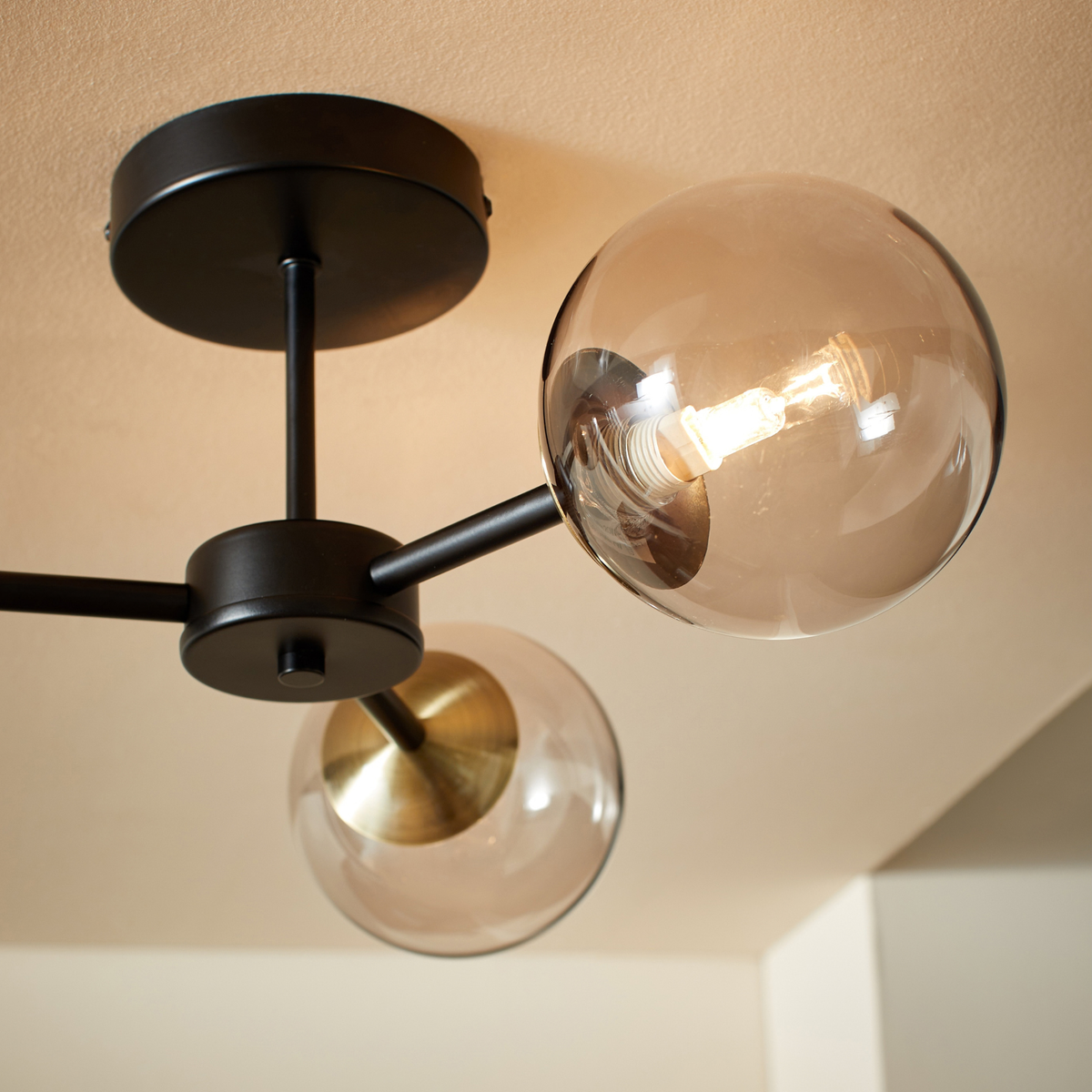 MADE Globe 3 light flush ceiling light close up of matt black canopy and tinted glass globe
