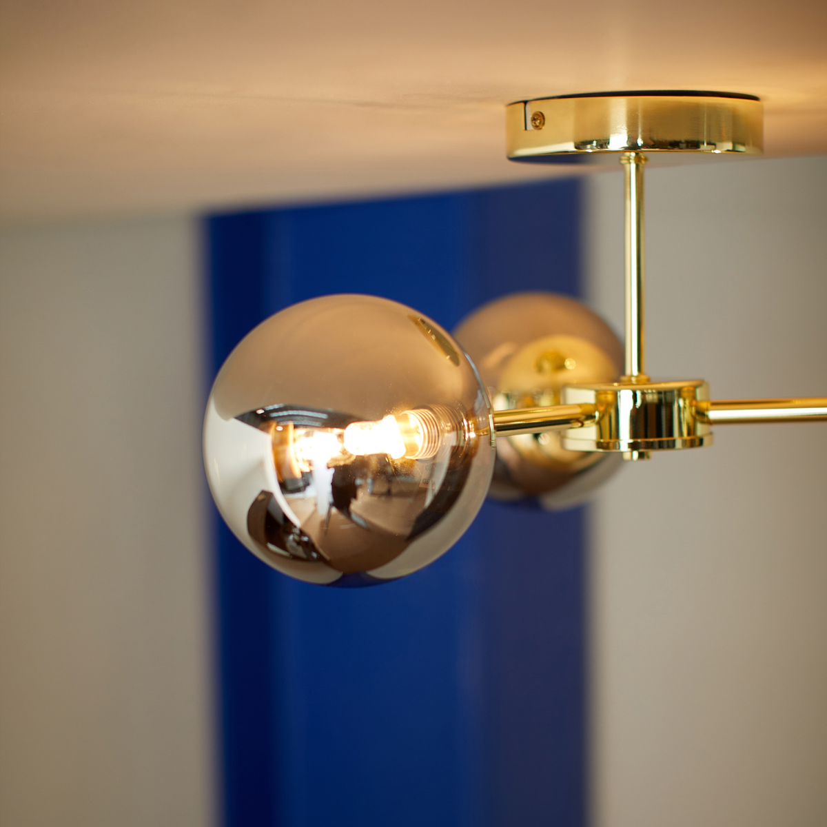 MADE.COM Globe 3 light flush ceiling light close up of a mirrored smoked glass shade and polished brass arm