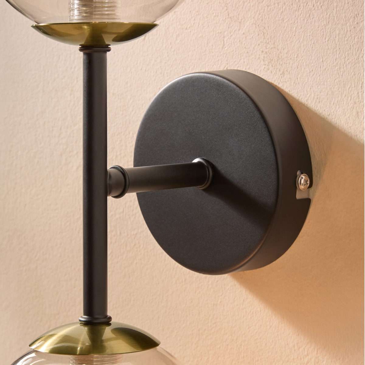 Close up of matt black wall plate, antique brass collar and clear glass globe on MADE.COM Globe wall light