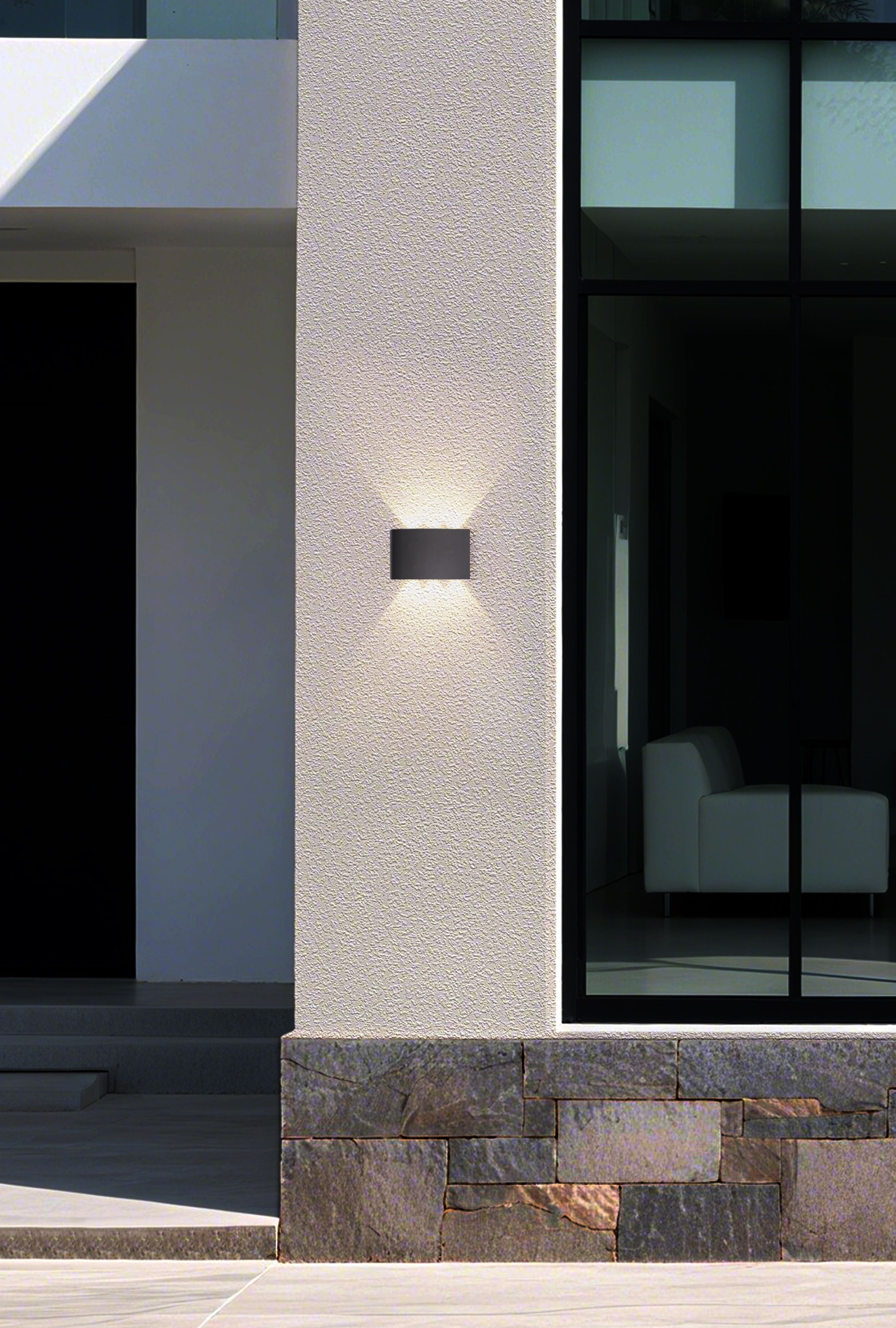 Shadows LED outdoor wall light 18cm mounted on a rendered house wall beside dark framed glazing, illuminated at dusk casting light up and down the wall