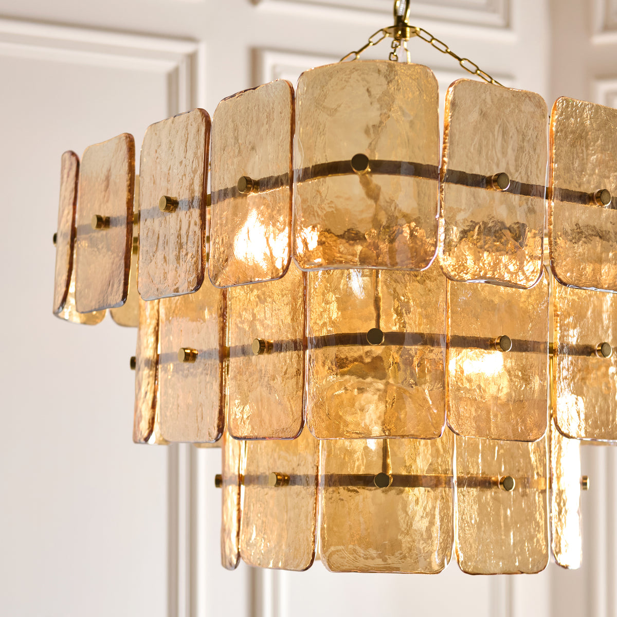 Close up detail of the Endon Venice 10 light pendant showing the tiered champagne textured glass panels and brass banding lit from within