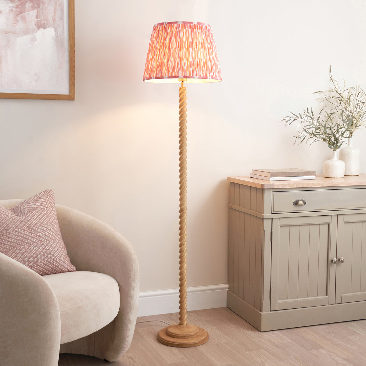 Endon Twist floor lamp lit in a living room, oak effect twisted stem and pink ikat shade beside a cream armchair and grey sideboard