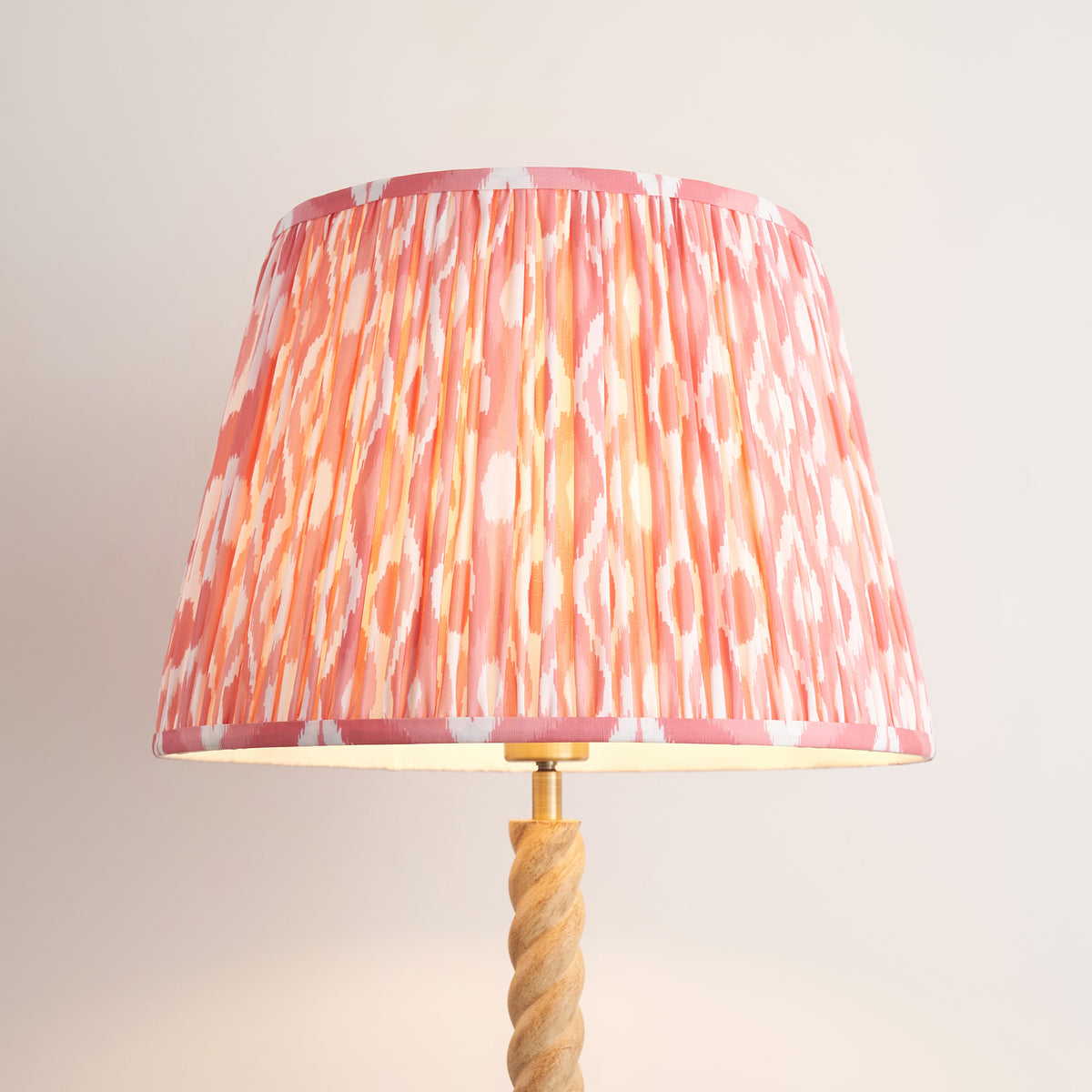 Close up of the lit coral pink ikat shade on the Endon Twist floor lamp, showing the pleats and brass coloured lamp holder