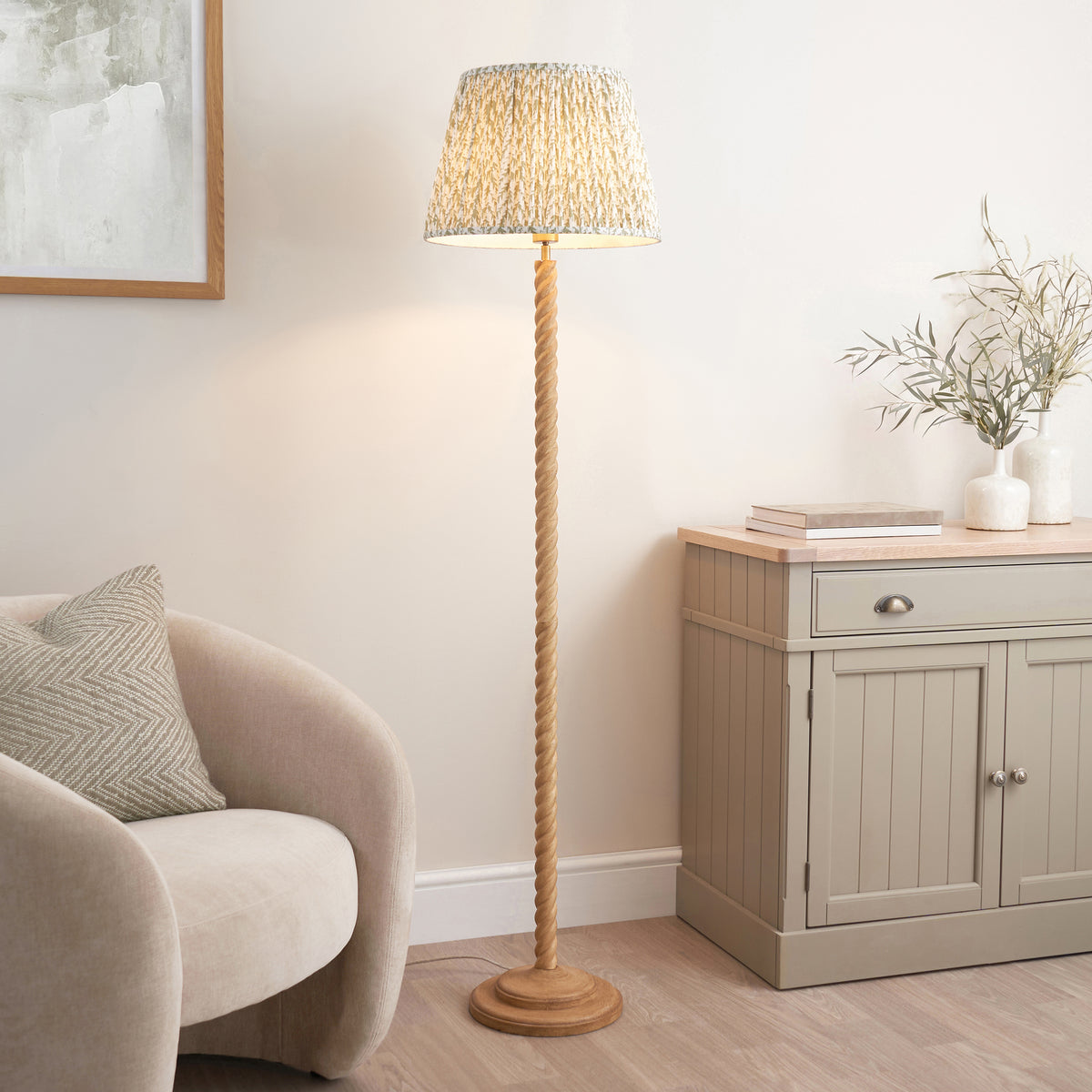 Endon Twist oak effect floor lamp with green leaf shade lit in a living room beside a cream armchair and grey painted sideboard