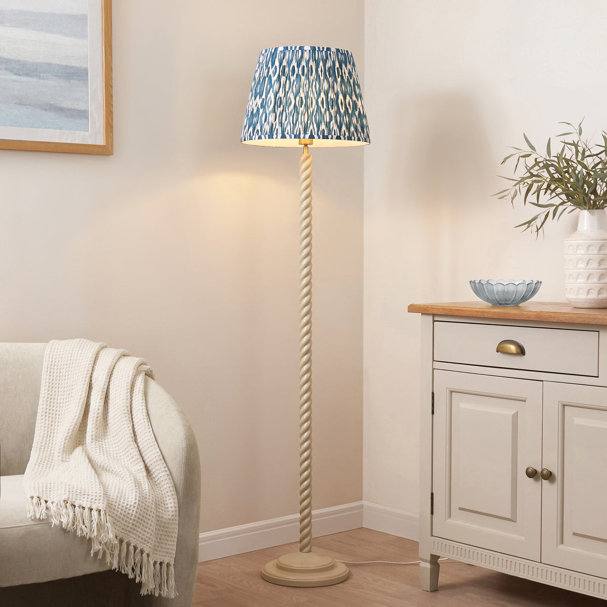 Endon Twist floor lamp with blue ikat shade switched on beside a cream armchair and a painted sideboard in a living room