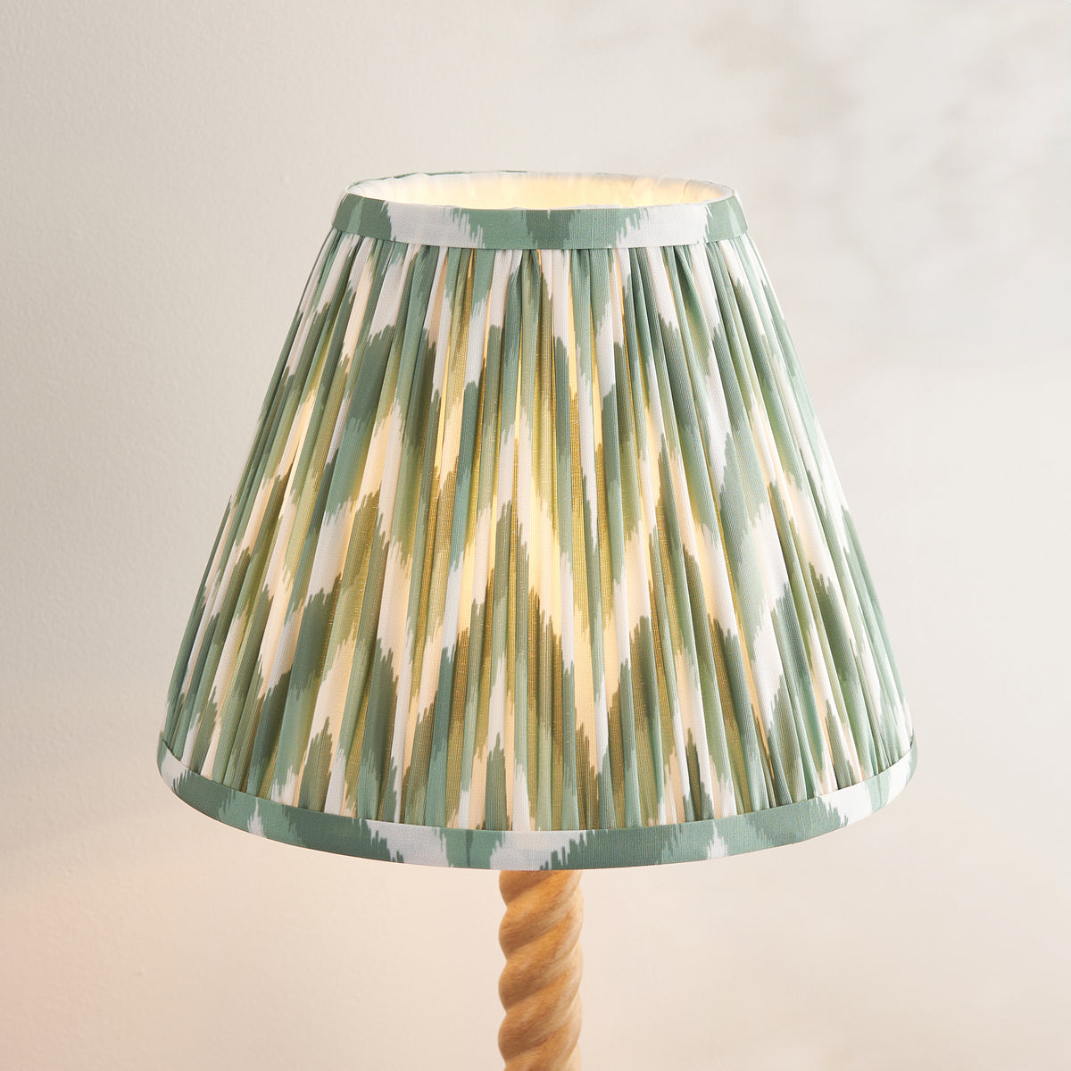 Close up of the lit Cotswold green zigzag pleated shade on the Endon Twist oak effect table lamp, showing the taped edge