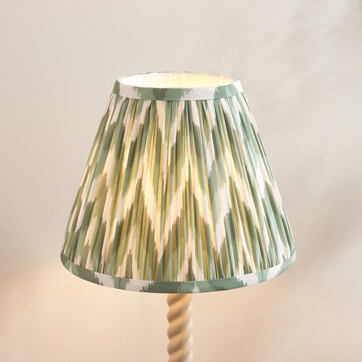 Close up of the lit Cotswold green zigzag pleated shade on the Endon Twist table lamp, top of the almond white twisted stem visible