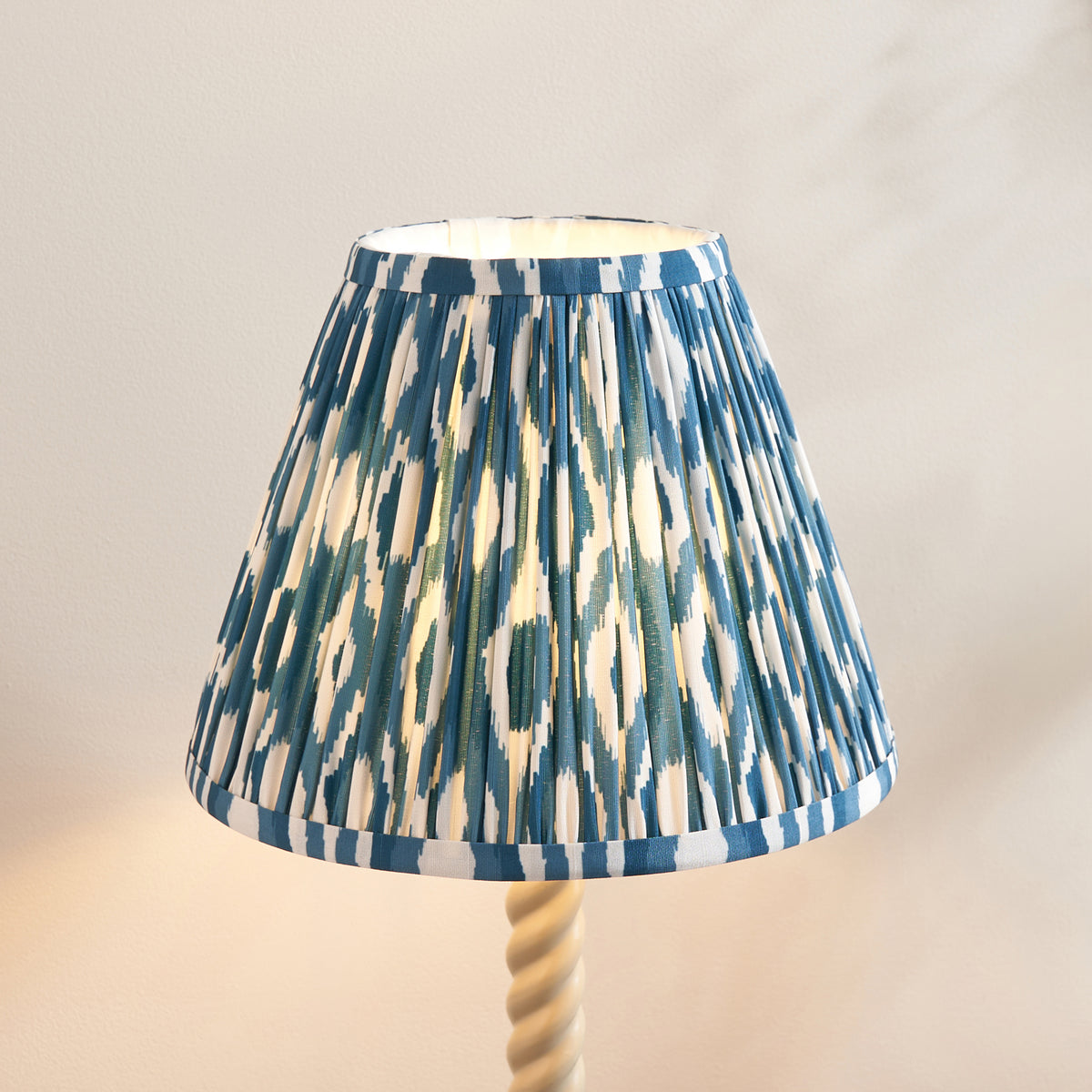 Close up of the Endon 25cm marlin blue ikat pleated shade, lit from inside, with the top of the white twisted stem below