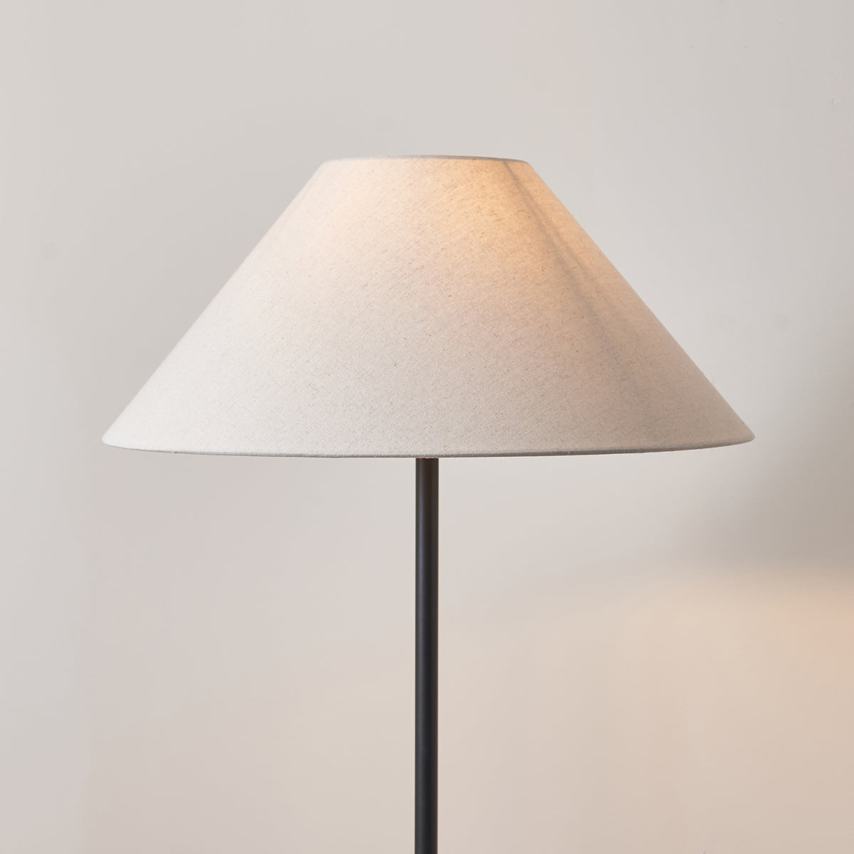 Close up of the Avalon 52cm natural linen coolie shade on the Endon Arlo floor lamp, lit against a pale wall