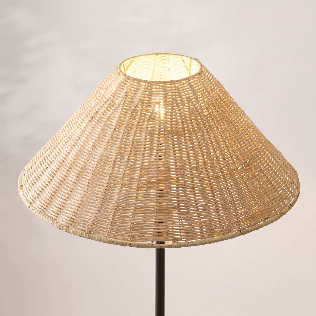 Close up of the lit natural rattan shade on the Endon Arlo floor lamp, showing the open weave and the black stem below