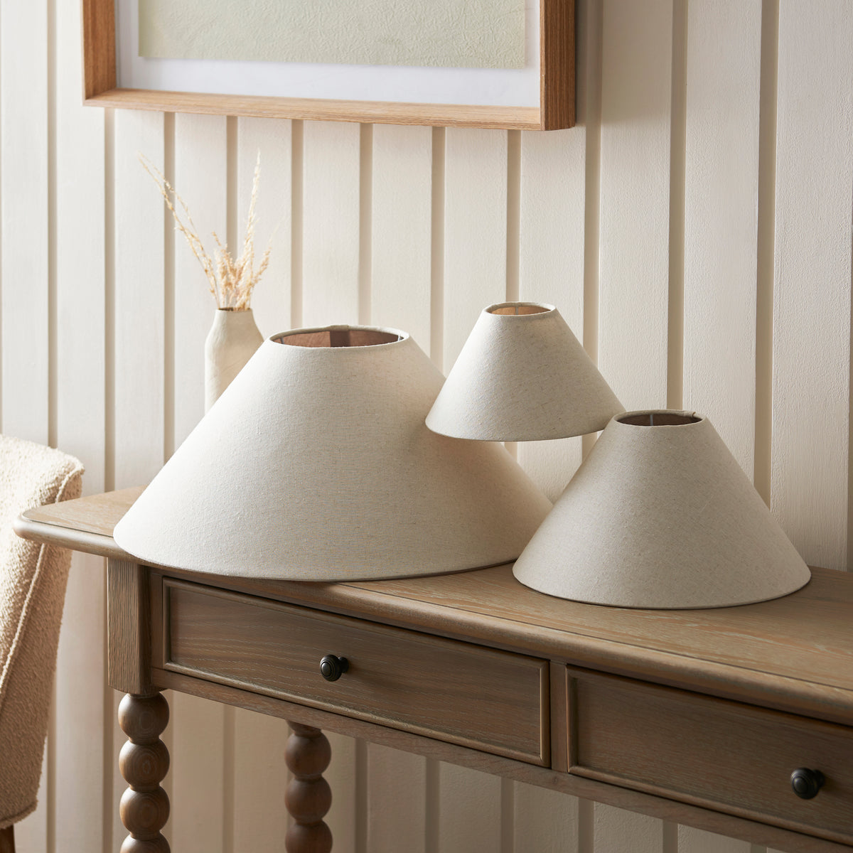 Three Endon Avalon natural linen coolie shades in different sizes on a wooden console table against a panelled wall, shade only shot
