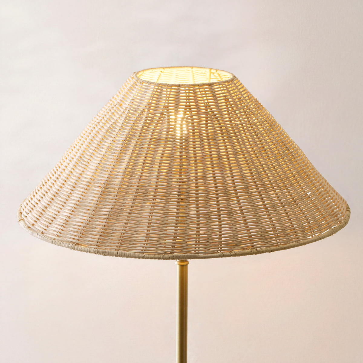 Close up of the Endon Arlo natural rattan shade lit from inside, showing the hand woven weave and antique brass stem below