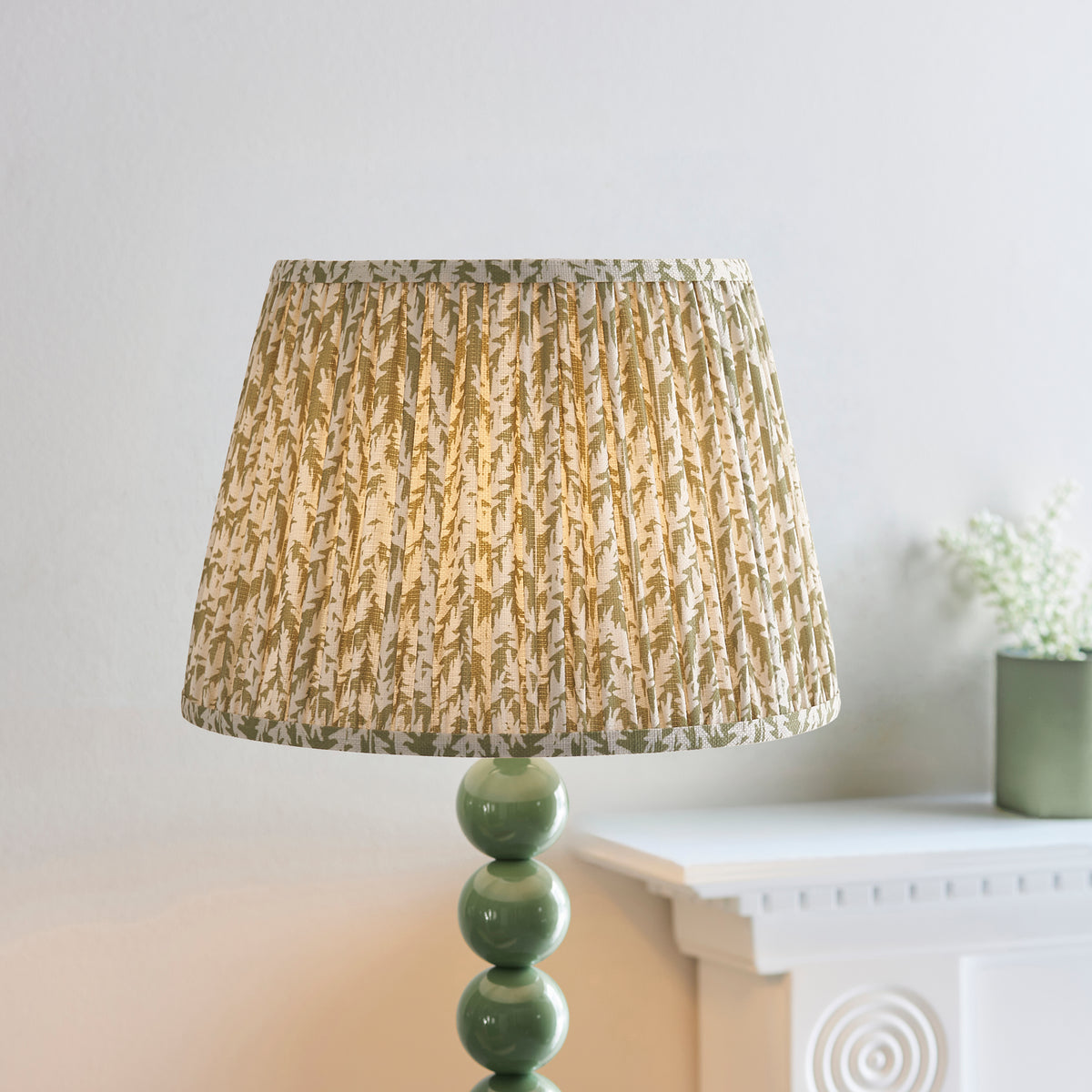 Close up of the lit pleated herb garden green leaf print Leaf shade on the Endon Higgledy floor lamp, white mantelpiece behind