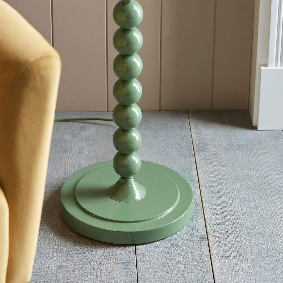 Close up of the round gloss Cotswold green base and lower spheres of the Endon Higgledy floor lamp on grey floorboards with green cable