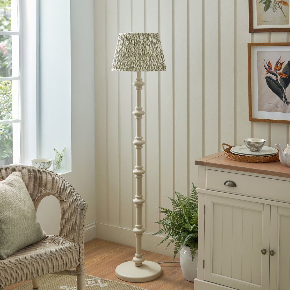 Endon Carnaby floor lamp unlit beside a window and rattan armchair, satin almond white stem with herb garden green pleated Leaf shade