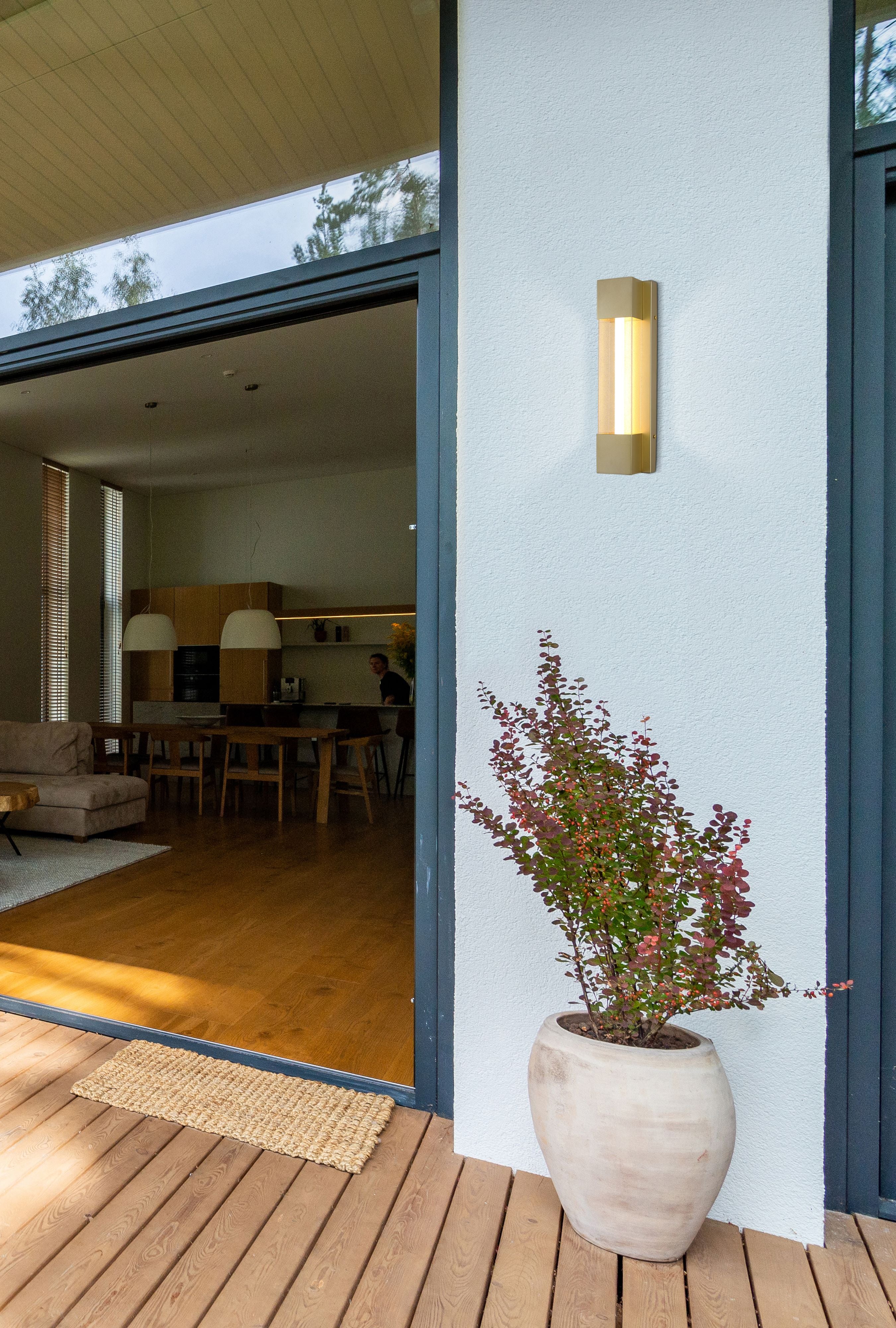 Sacramento outdoor LED wall light in painted gold installed beside a patio door on an exterior wall, lit at dusk