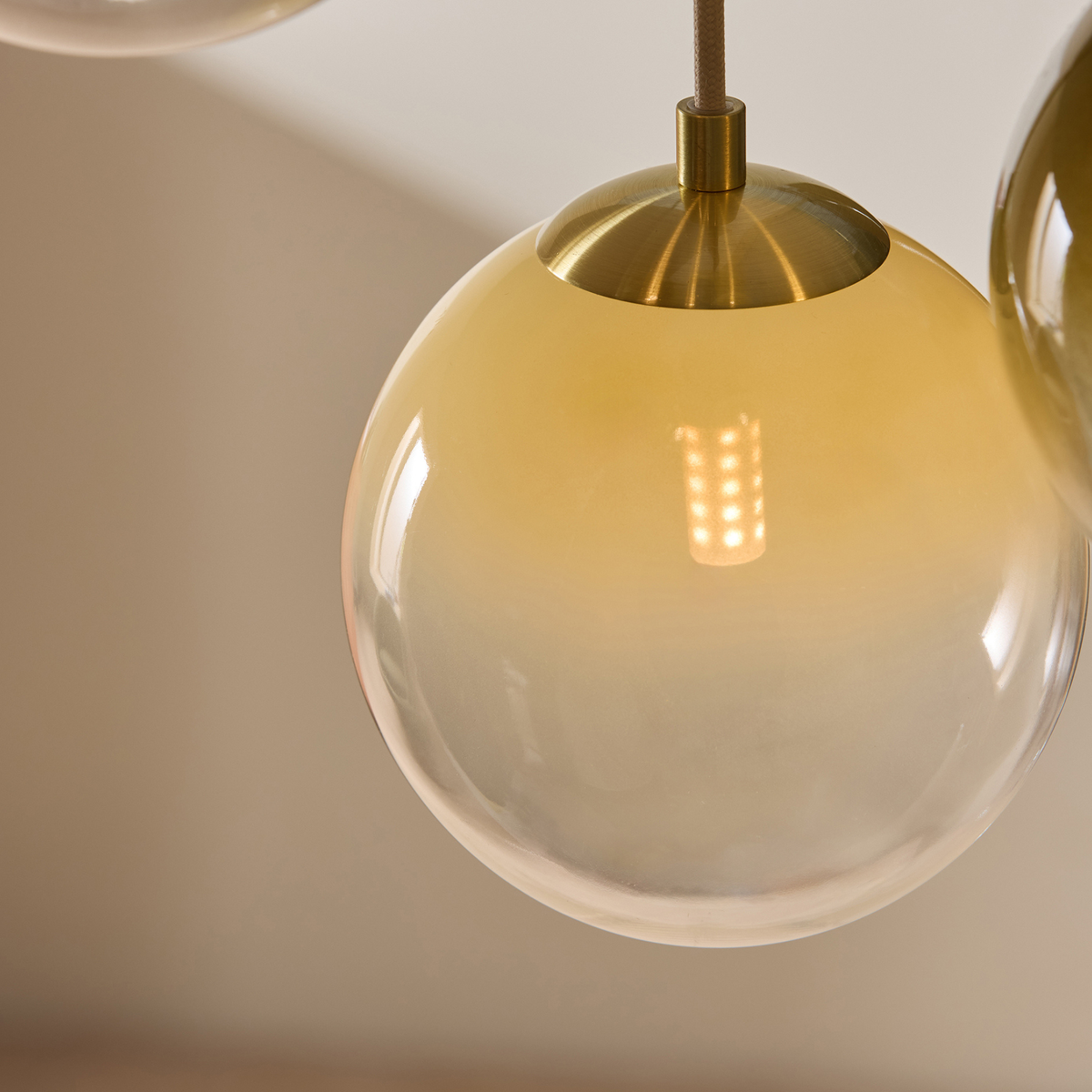 MADE.COM Globe pendant ombre glass globe fading from amber to clear with brass cap, close up