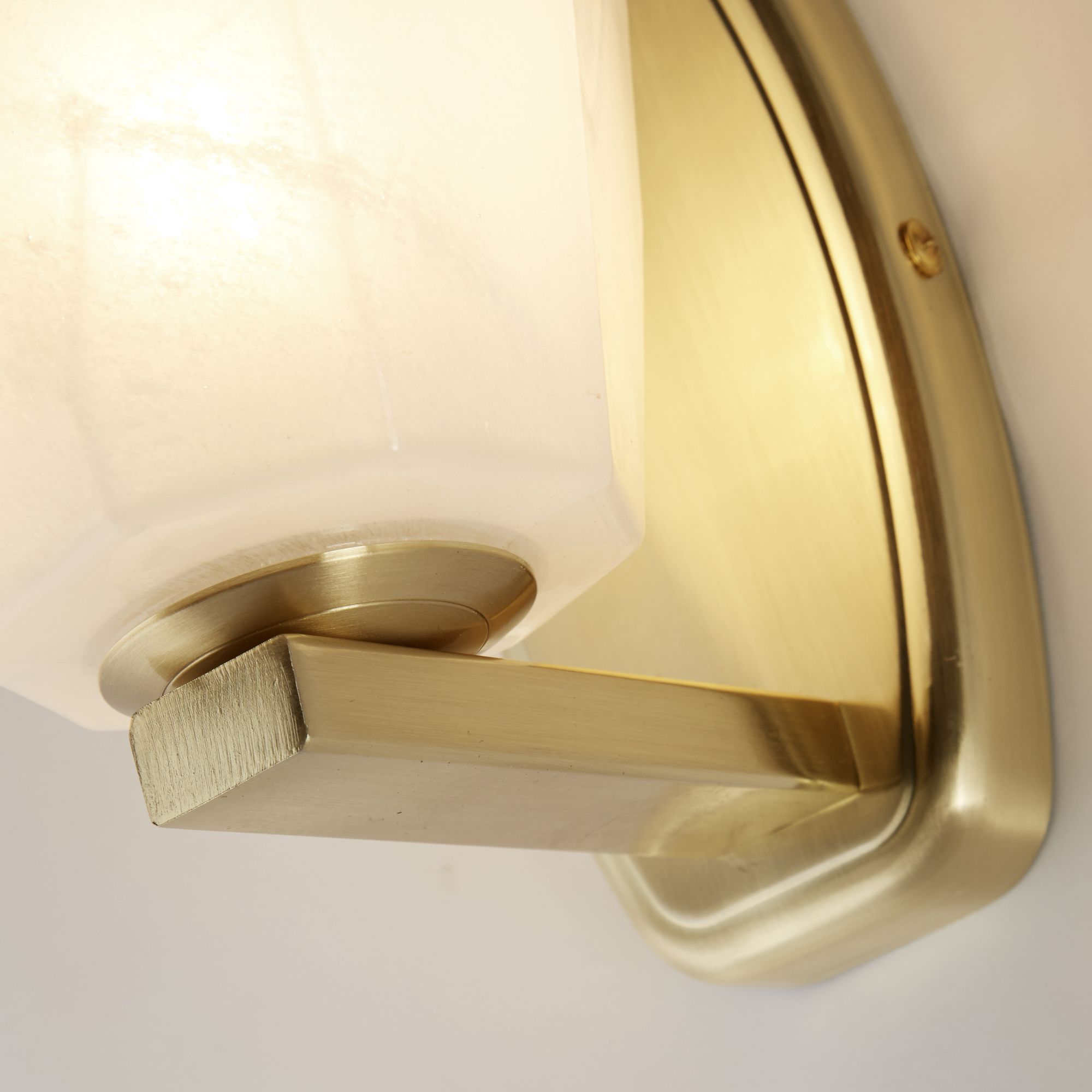 Close up of the Rocky wall light's satin brass bracket and fixing detail against the faceted glass shade