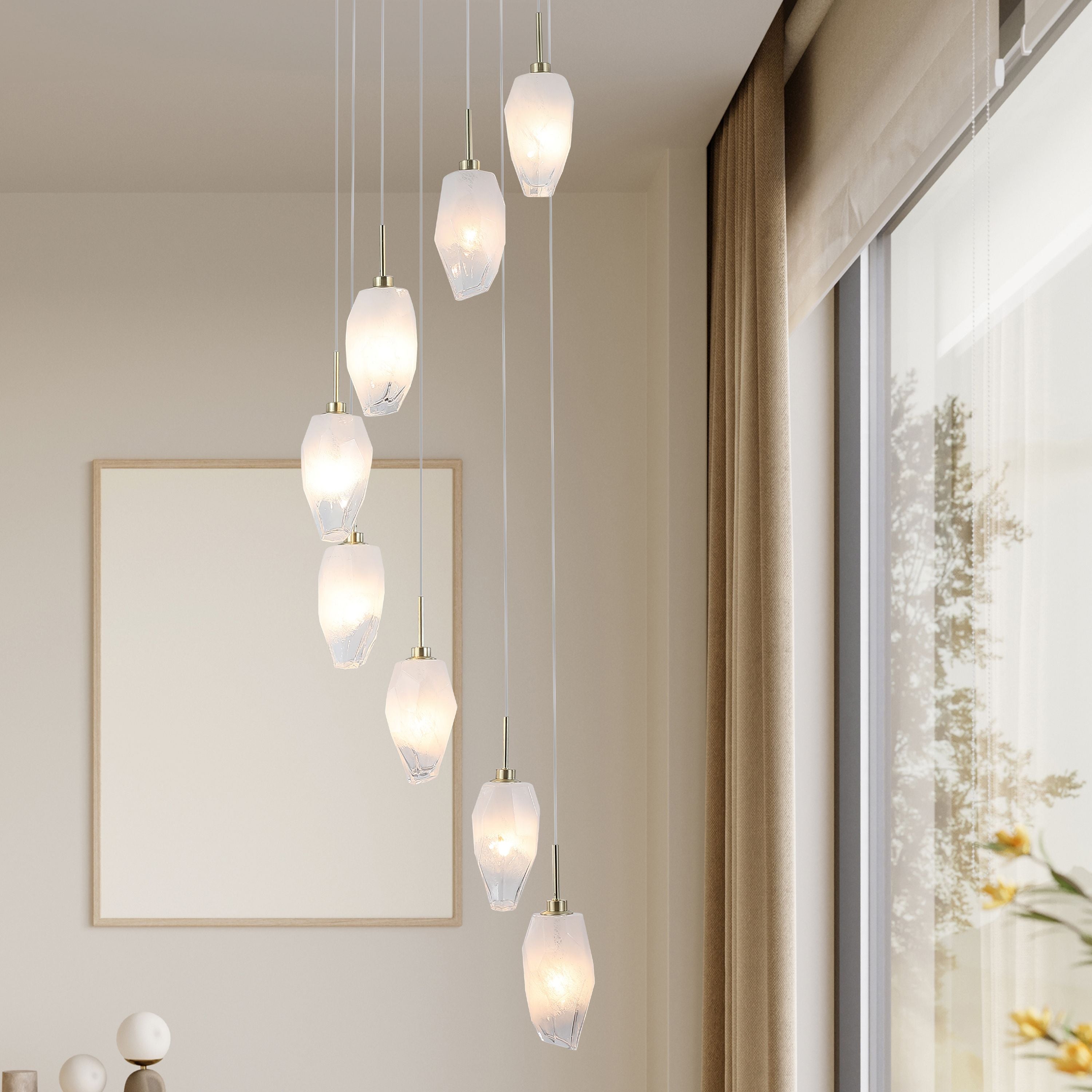 Rocky 8 light pendant in satin brass styled cascading in a living space beside a window, shades illuminated with a warm glow