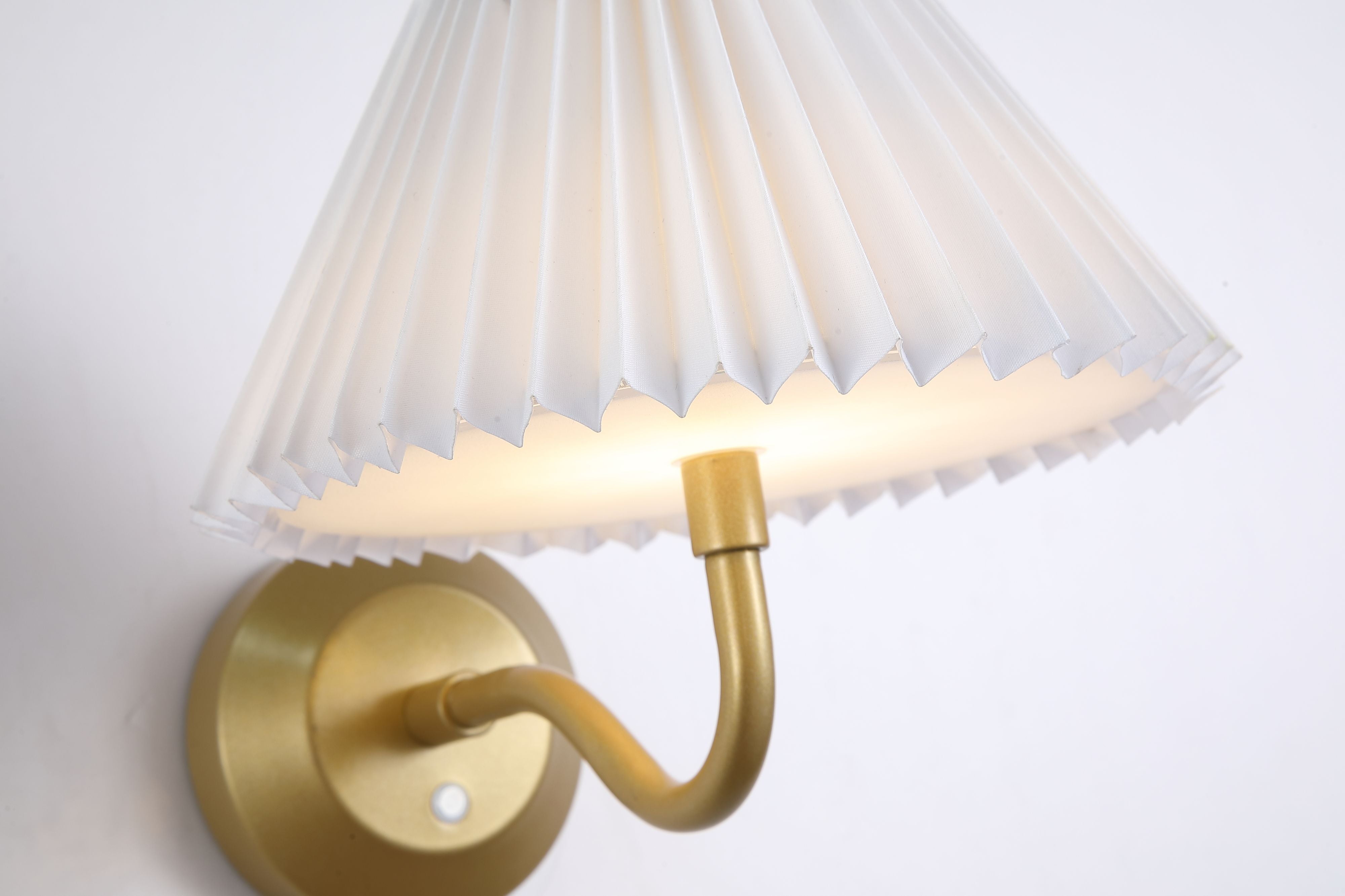 Close up of the Danish wall light's pleated white shade and curved gold arm, showing the fabric folds and warm LED glow