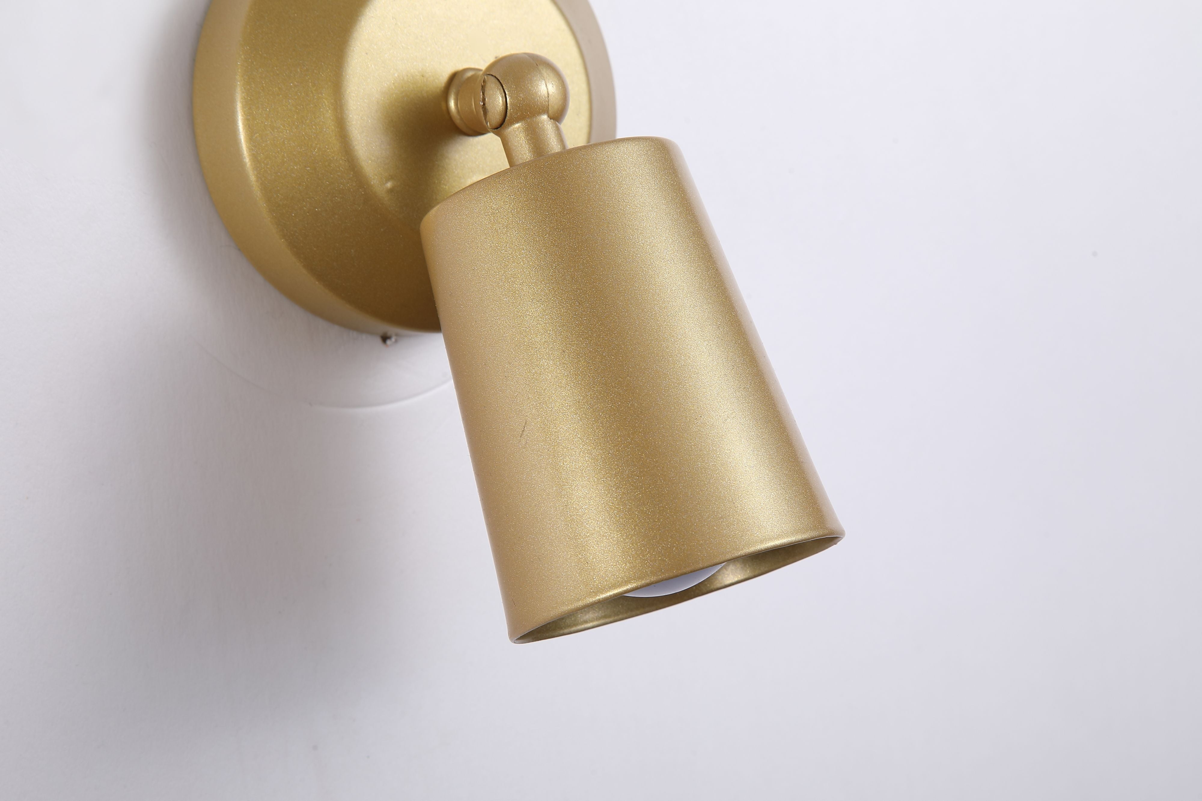 Close up angled view of the gold Cone wall light showing the ball joint swivel and cylindrical shade against a plain wall