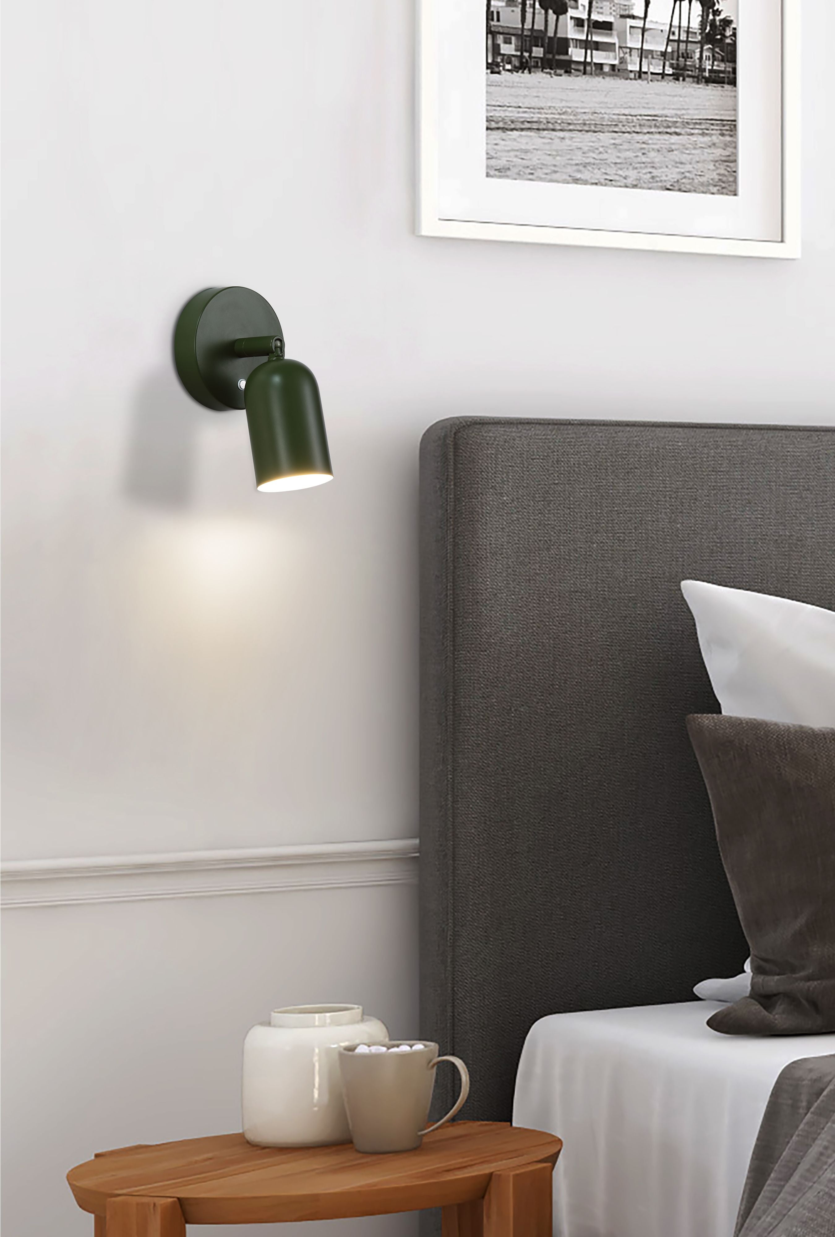 Green Cone wall light mounted on a white bedroom wall beside a dark grey headboard, below a black and white framed photograph