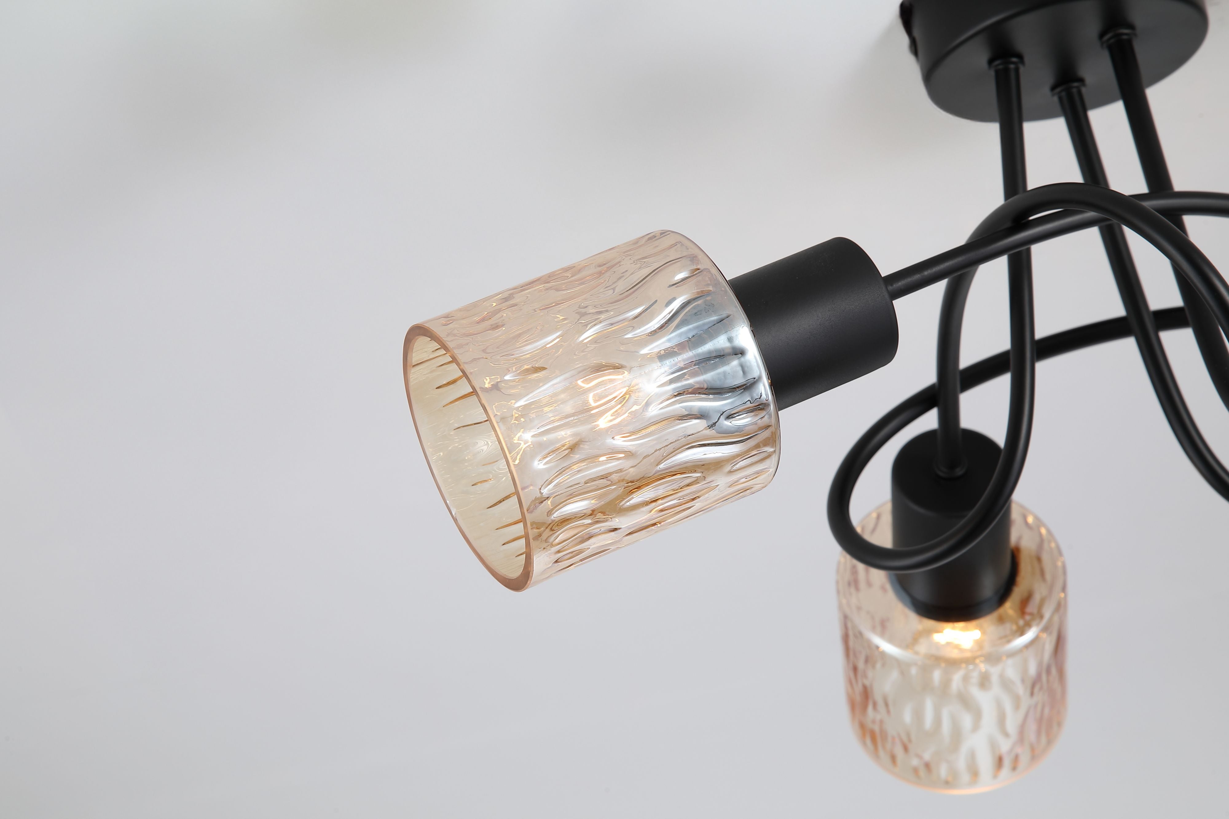 Close up of the Knot ceiling lamp's rippled amber glass shade and looping black metal arms