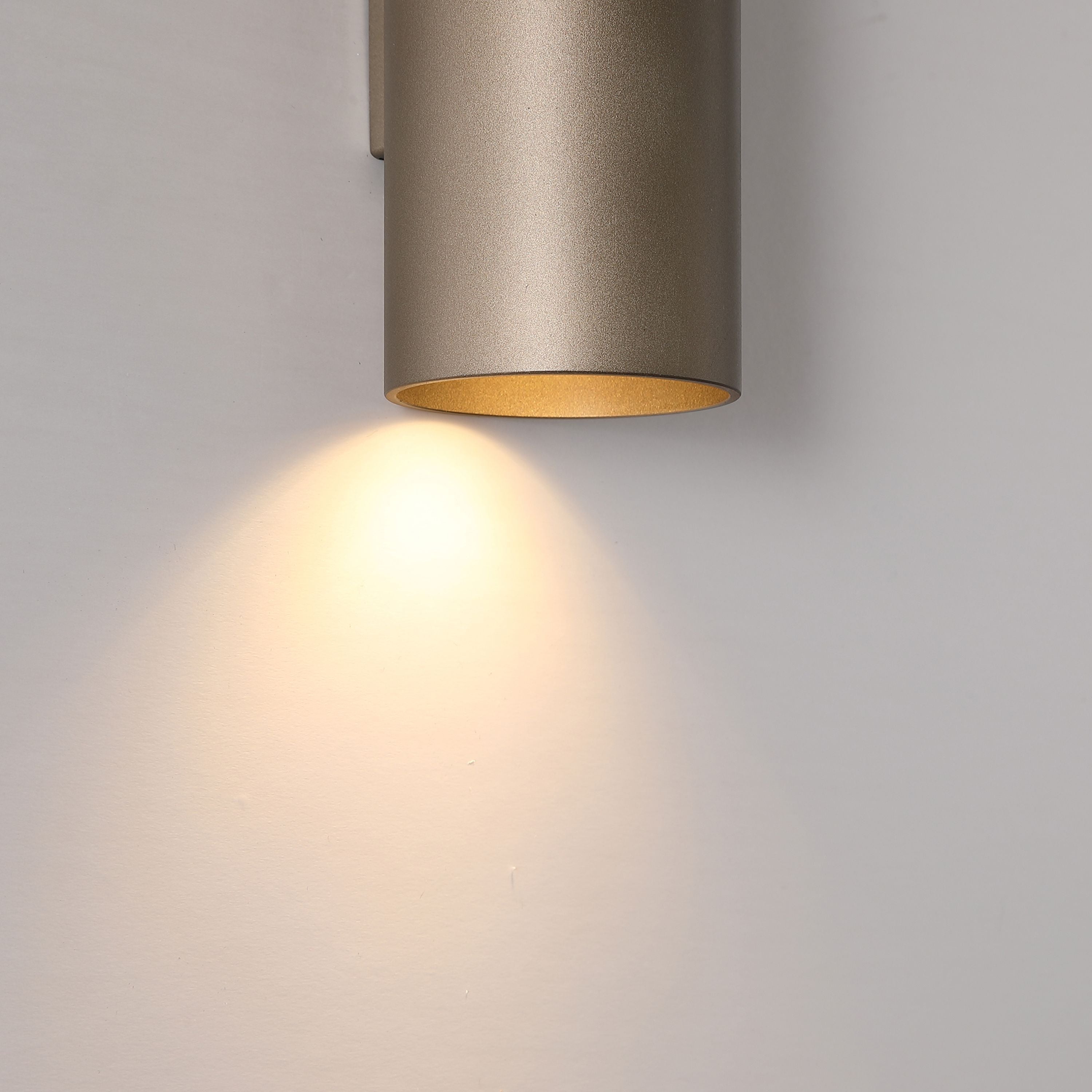 Close up of the Searchlight Cyls wall light in latte finish showing the matte texture and lit lower aperture against a grey wall