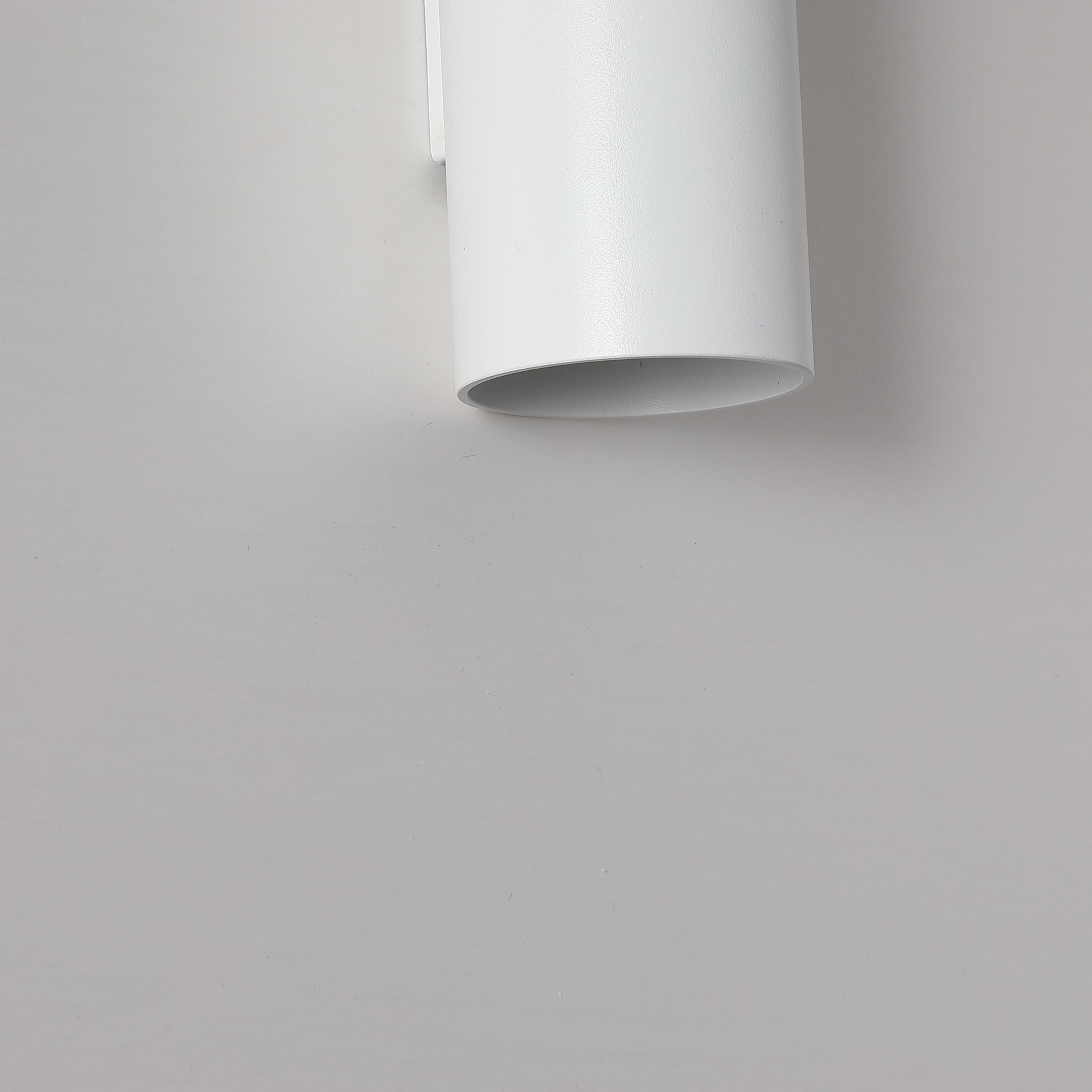 Close up of the Searchlight Cyls wall light in white showing the matte finish and unlit lower aperture against a grey wall