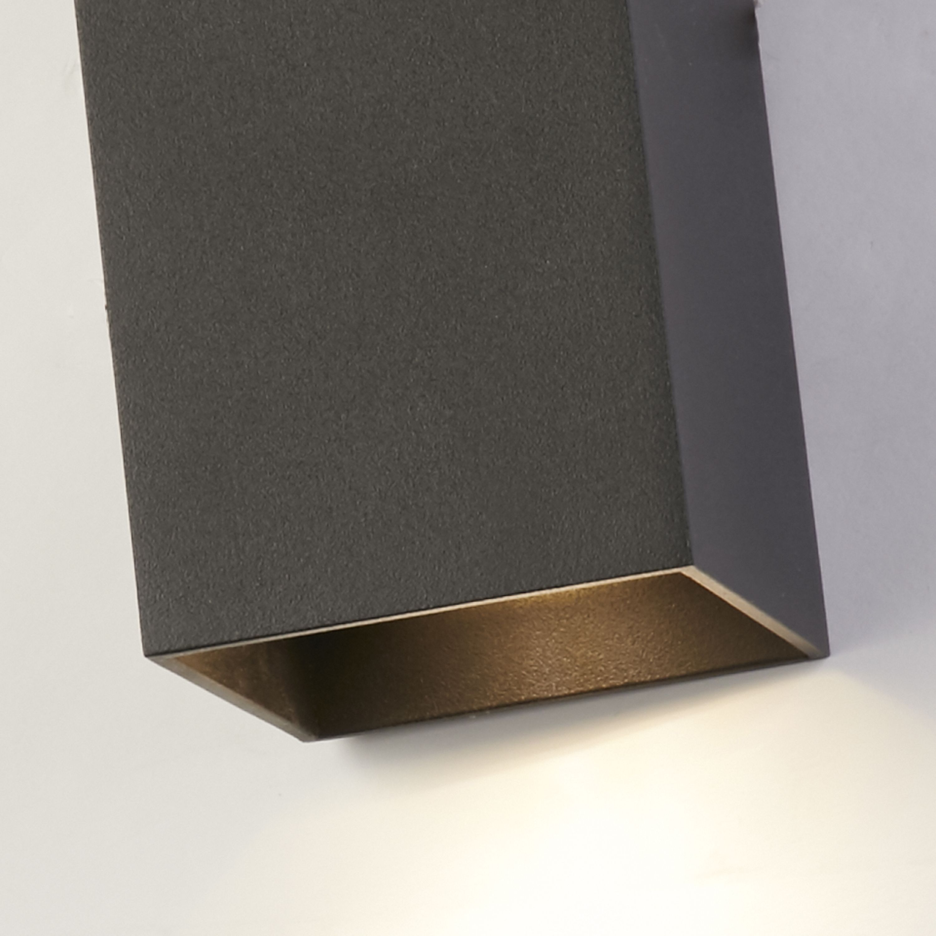 Close up of the Searchlight Don wall light in matte black showing the warm brass toned interior of the bottom light channel