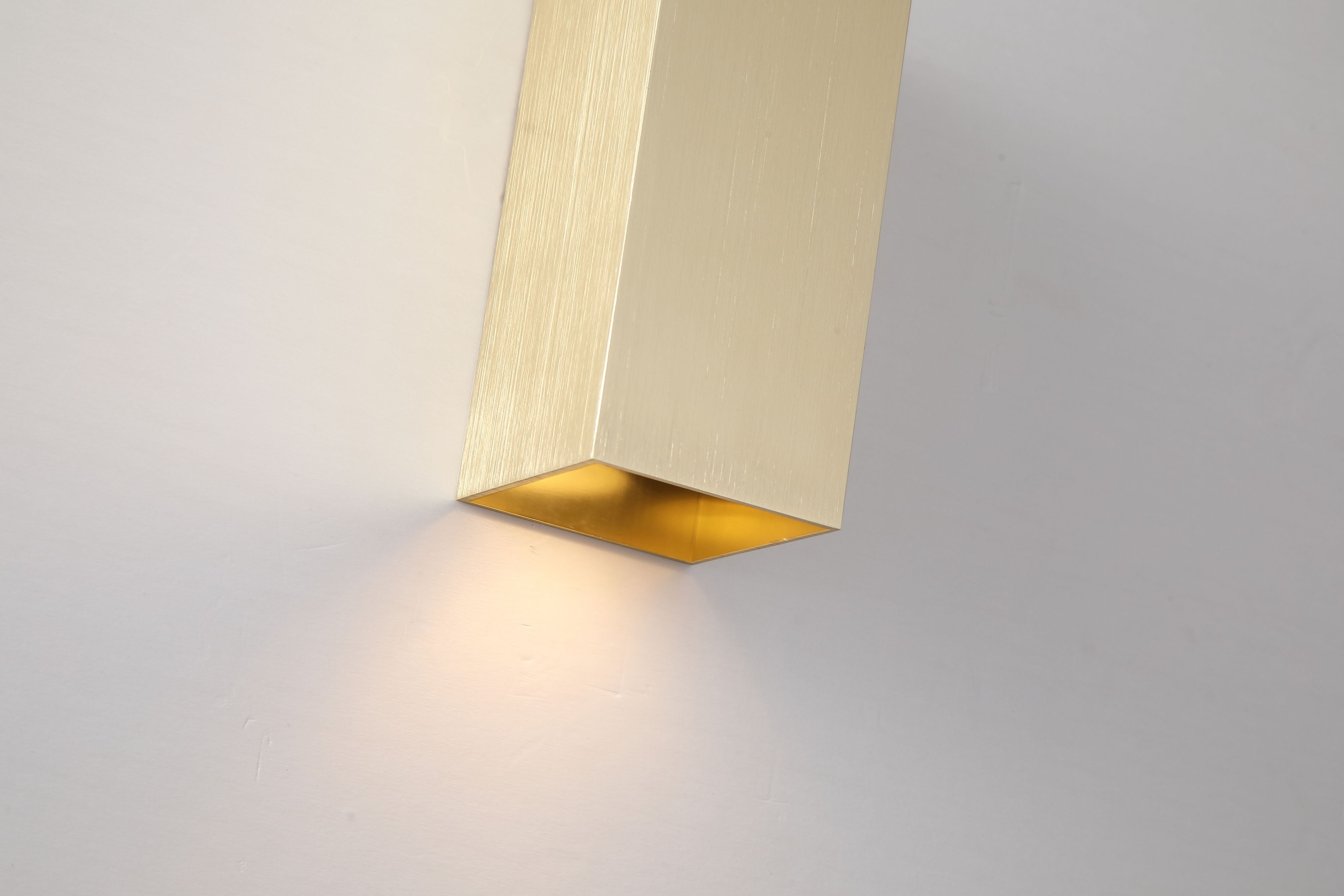Close up of the Searchlight Don wall light in brushed gold showing the gold toned interior of the bottom light channel and lit glow