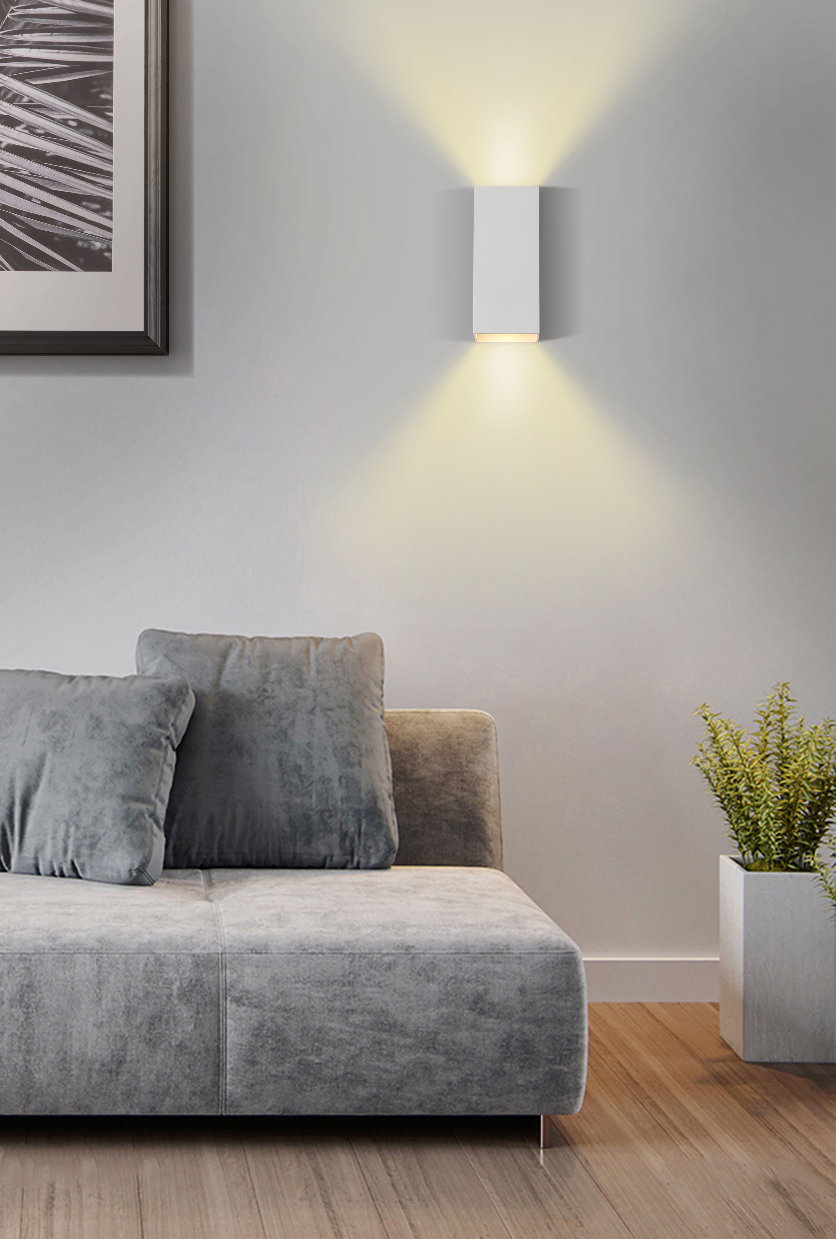 Searchlight Don wall light in matte white installed above a grey sofa, lit and casting light both upward and downward