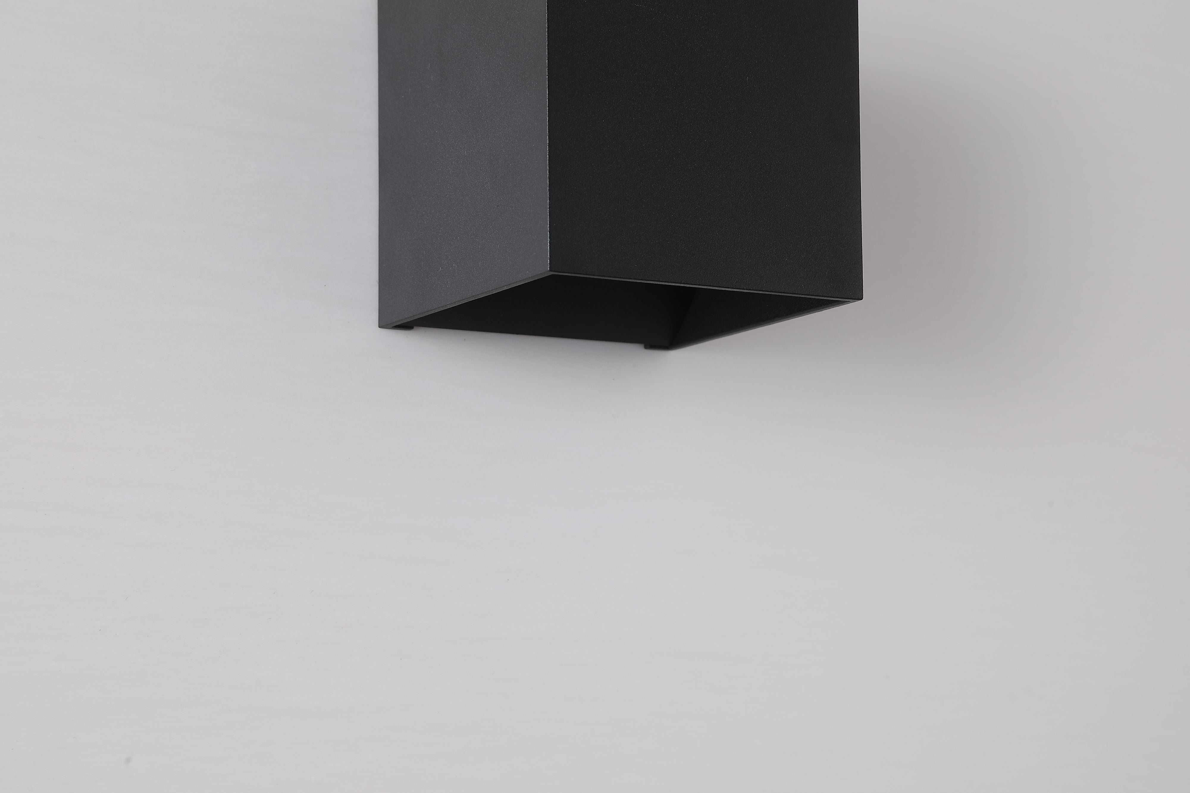 Close up of the underside of the Newton Square wall light in matte black, showing the angled slot where light spills downward