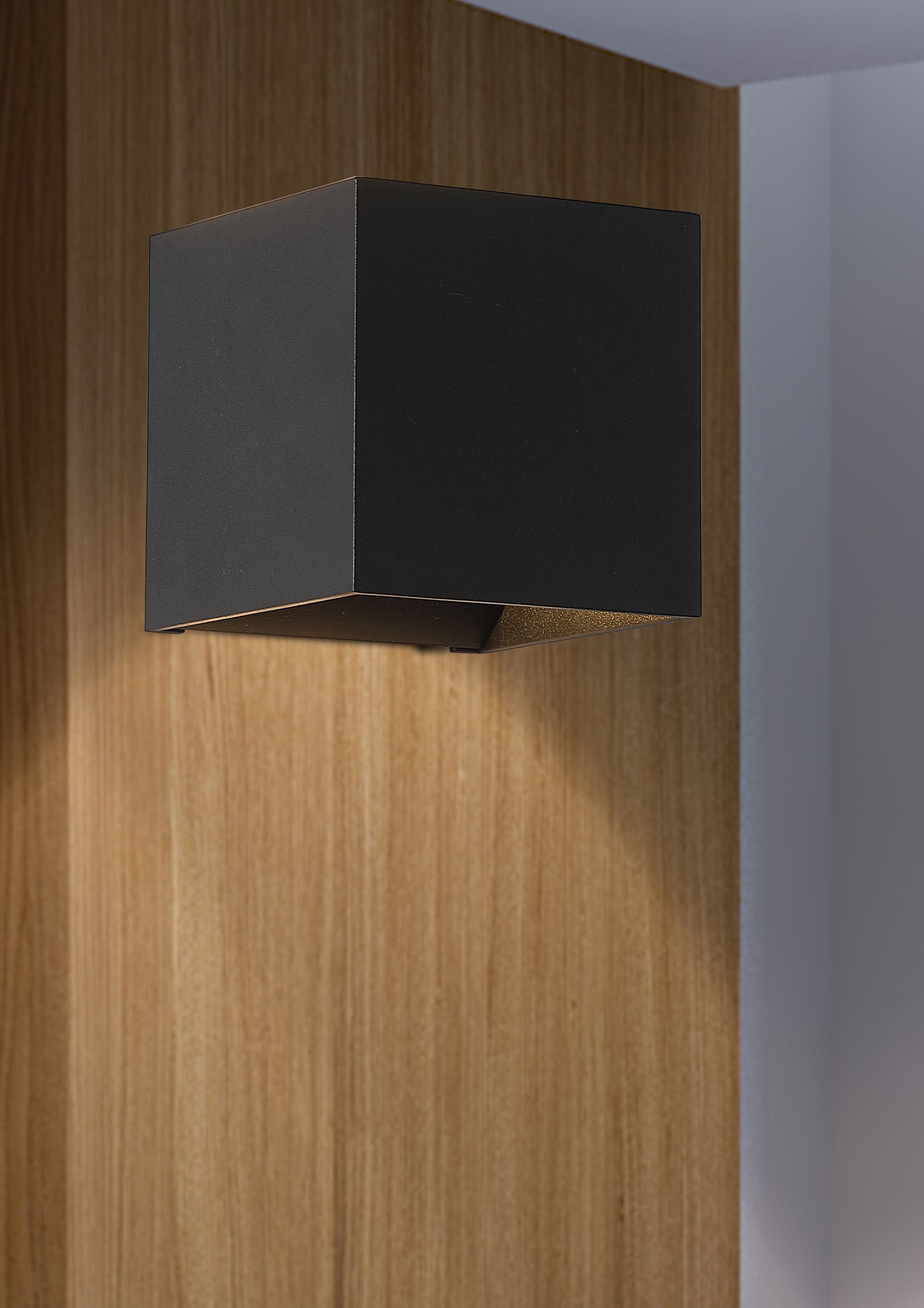 Newton Square Up & Down Wall Light in matte black installed on a wood panelled wall, glowing with warm light above and below the fitting