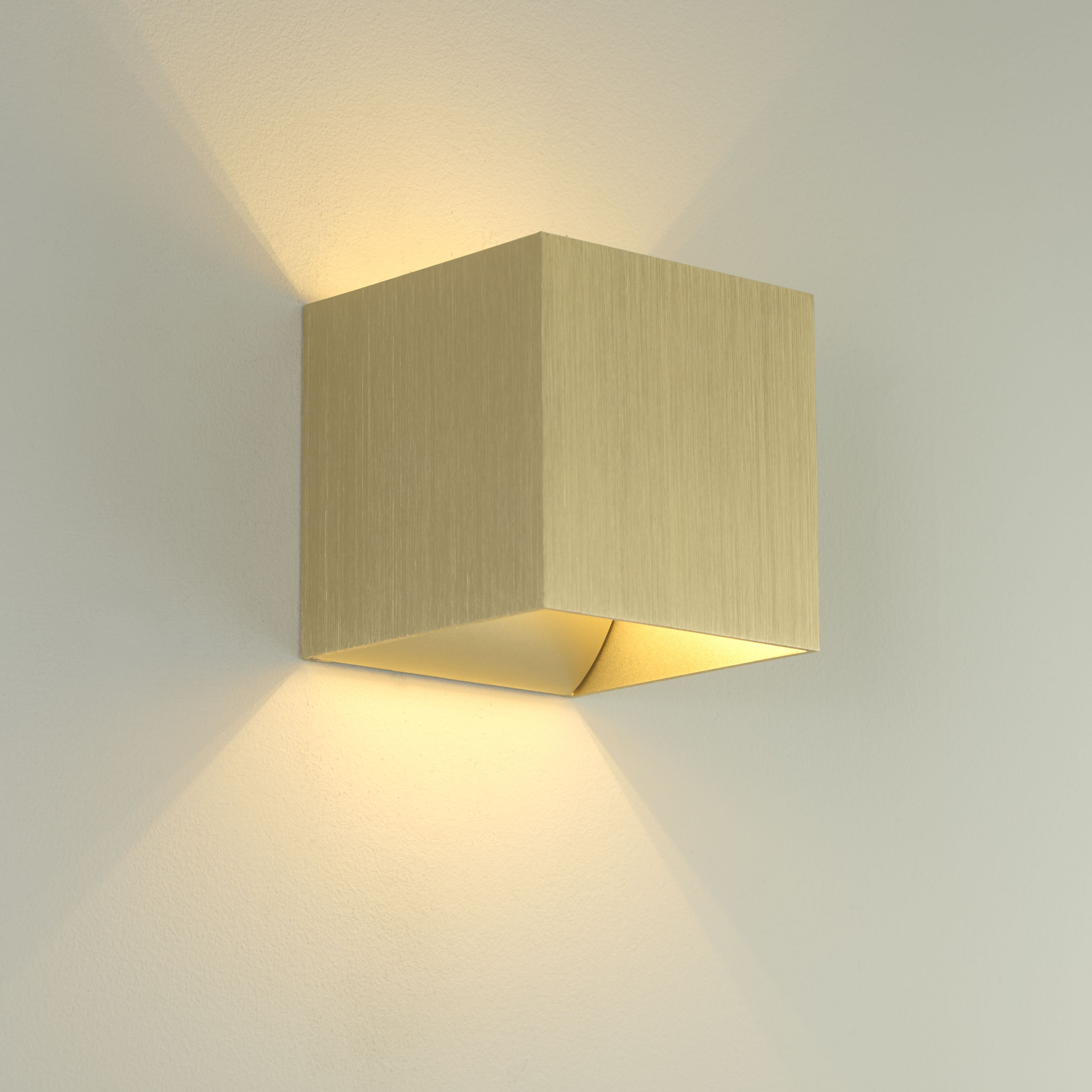 Newton Square Up & Down Wall Light in anodised gold installed on a wall, glowing with warm light above and below the fitting