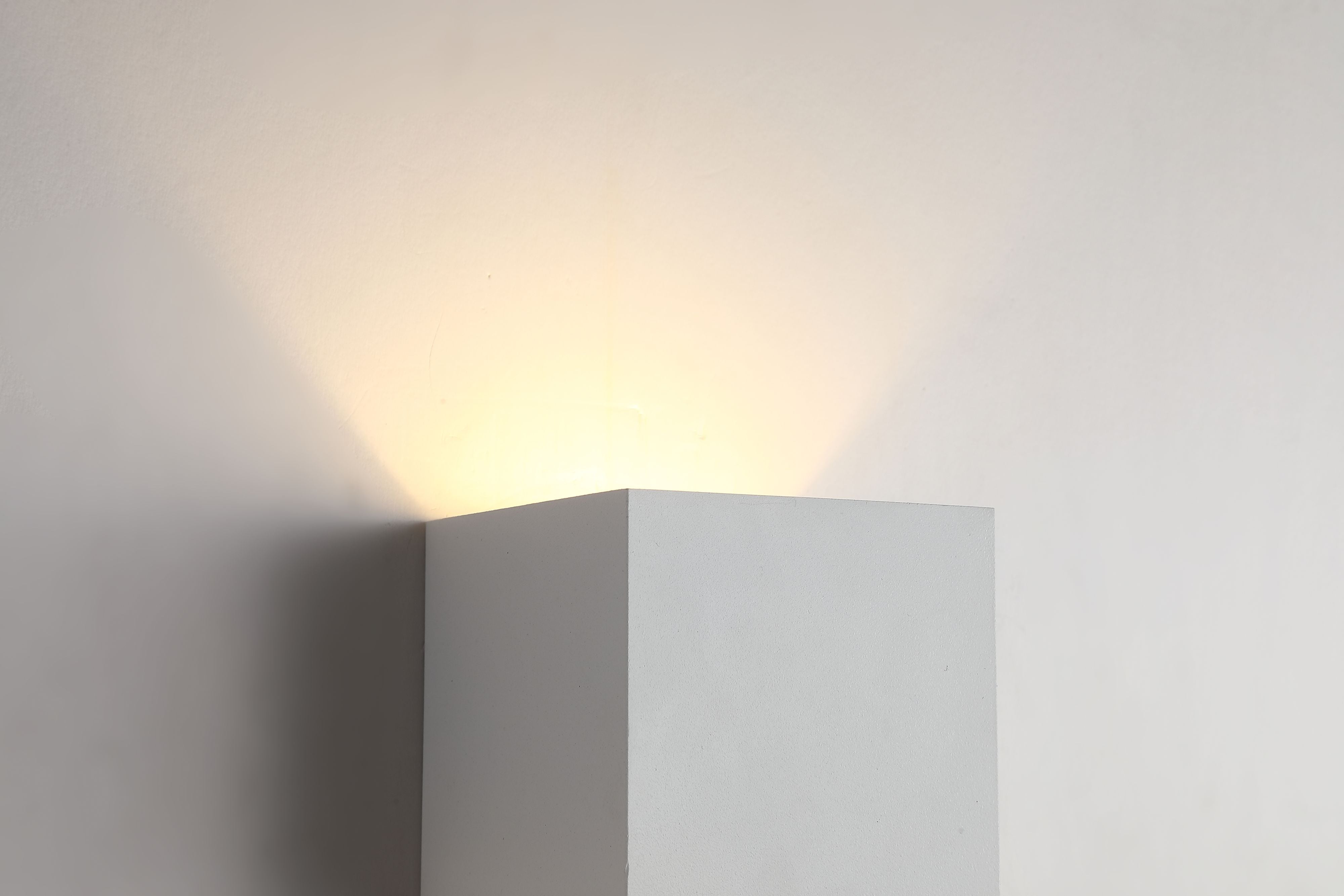 Close up of the top edge of the Newton Square wall light in sand white, showing warm light spilling upward from the fitting