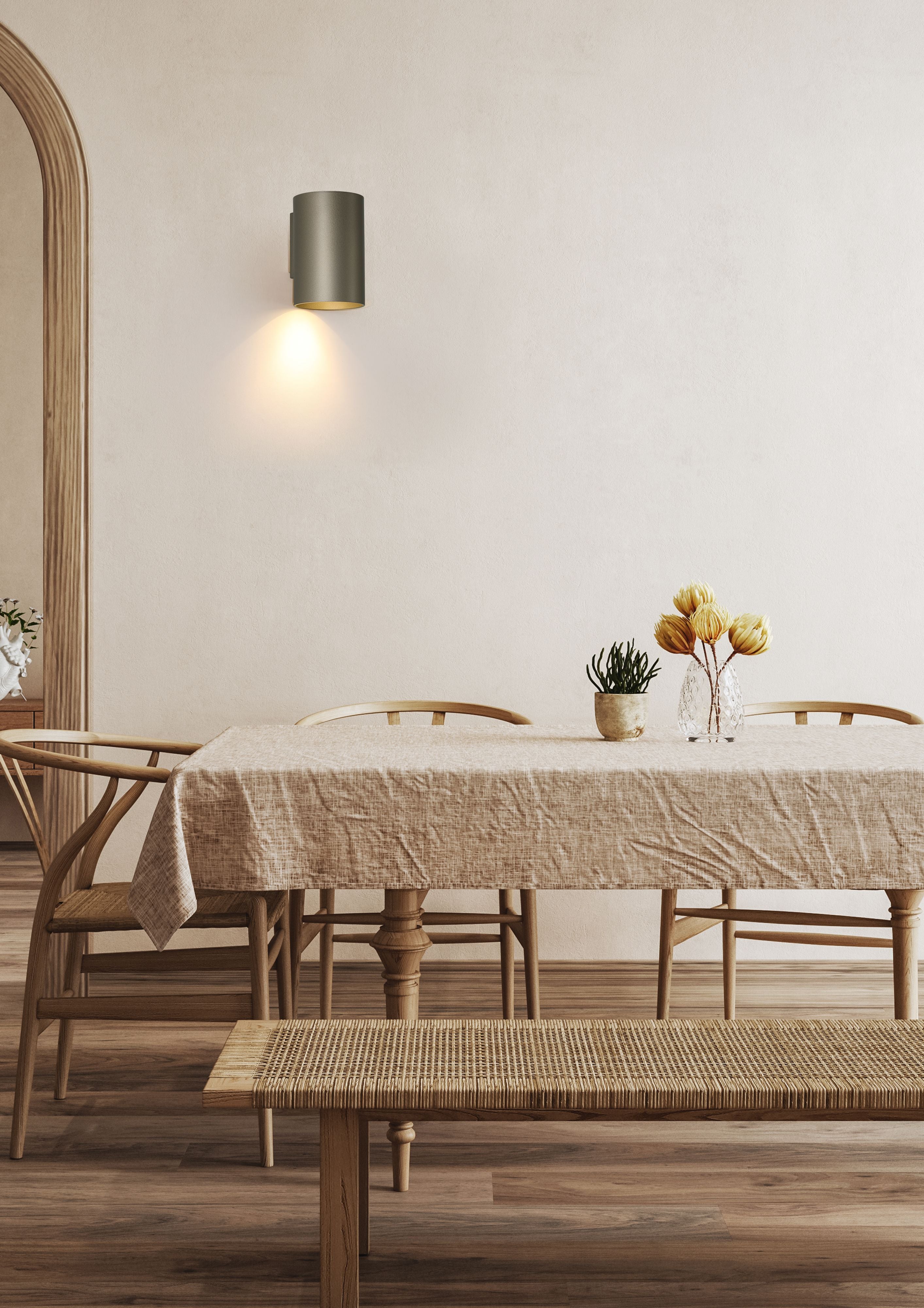 Searchlight Cyls Cylinder Down Wall Light in latte shown mounted alone on a wall in a styled dining area with an arched doorway, wood furniture and a rattan bench, light on