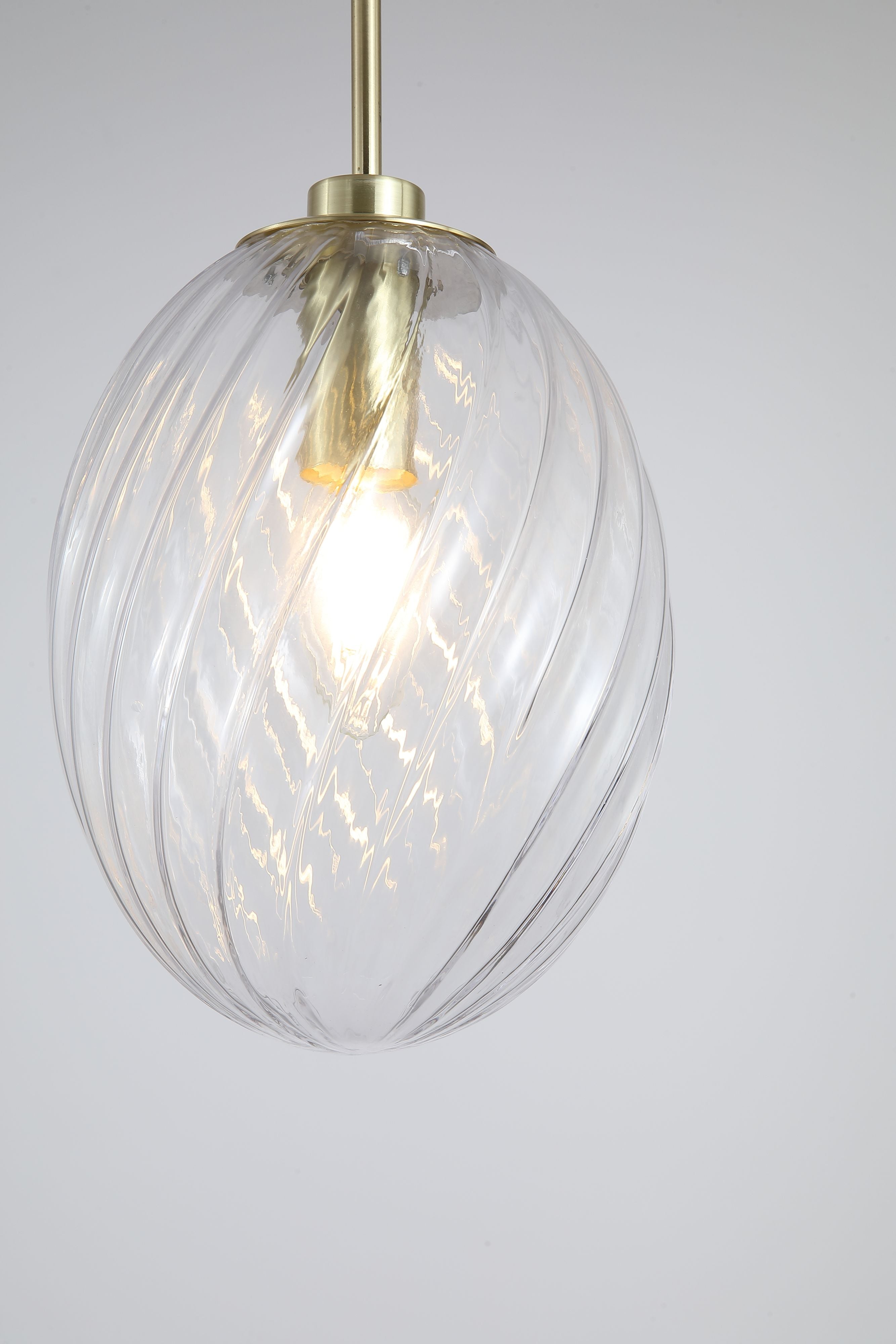 Close up of the ribbed swirl texture on the clear glass shade of the Whirl 1 Light Pendant, showing the satin brass gallery and bulb detail