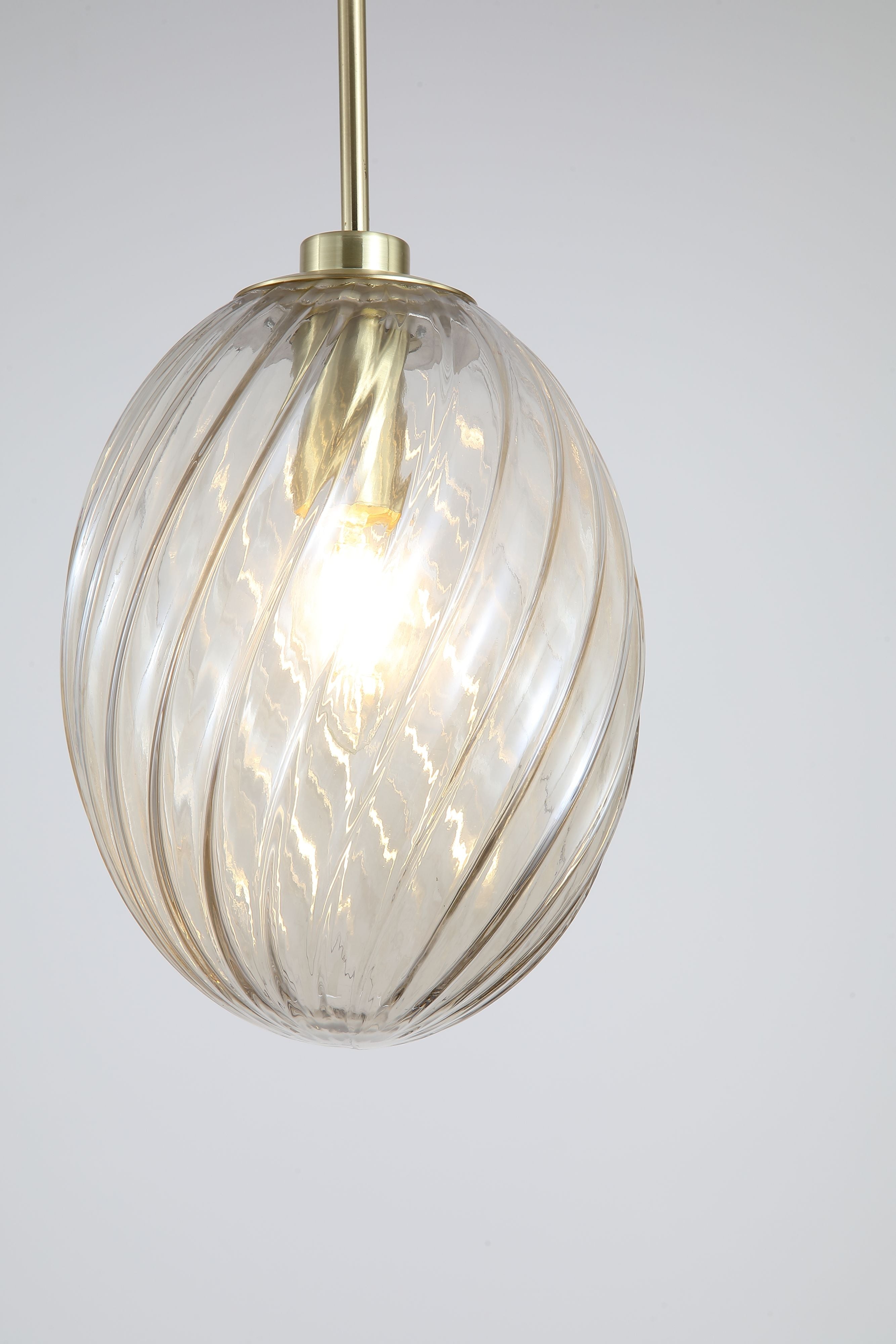 Close up of the champagne tinted swirled glass shade on the Searchlight Whirl pendant, showing the ribbed spiral texture, satin brass gallery and lit bulb inside
