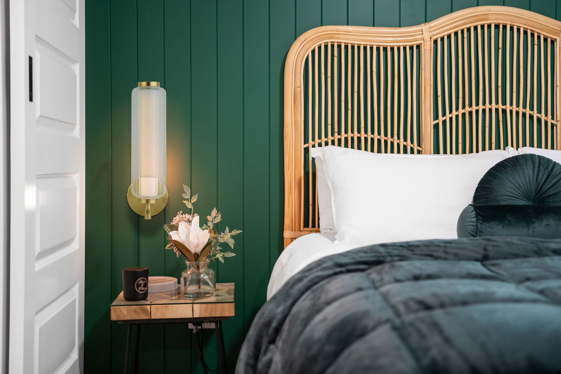 Searchlight Mod LED wall light mounted above a bedside table against a dark green panelled wall, styled bedroom with rattan headboard